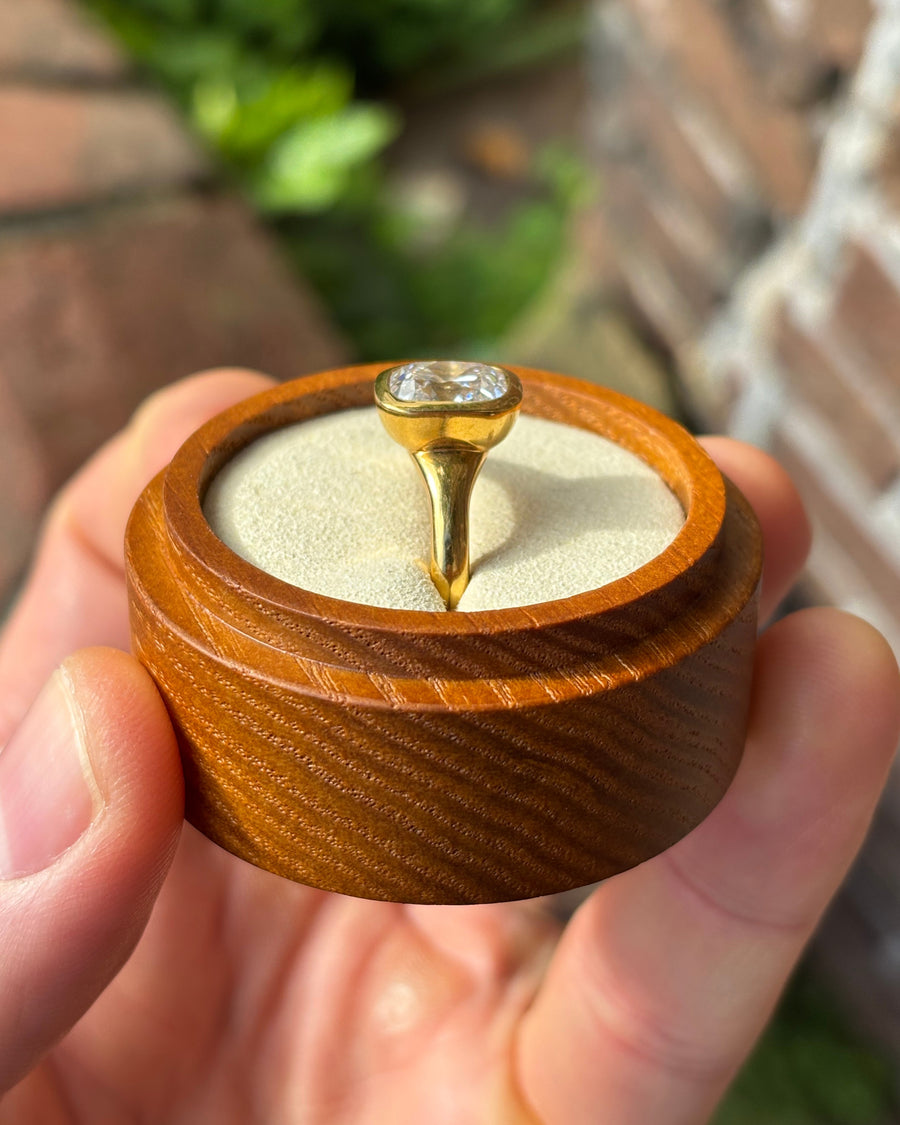 Cushion cut diamond engagement ring in a gold bezel setting held in a small wooden box.