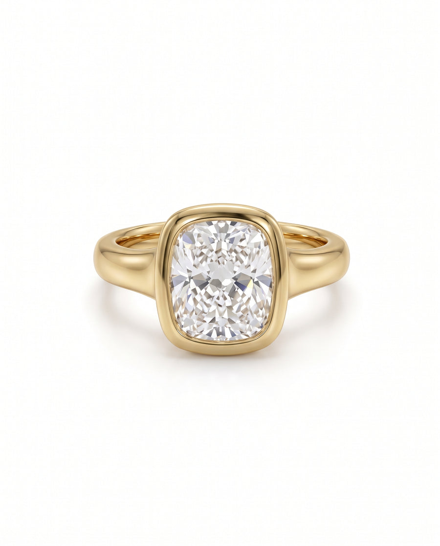 Cushion cut diamond engagement ring in a yellow gold bezel setting on a white background.