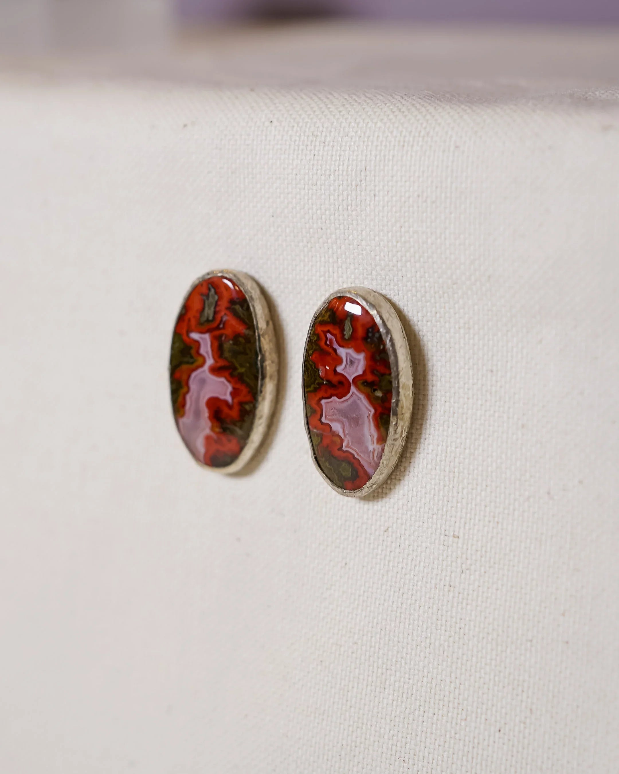 Handmade oval red gemstone stud earrings with silver setting on fabric background