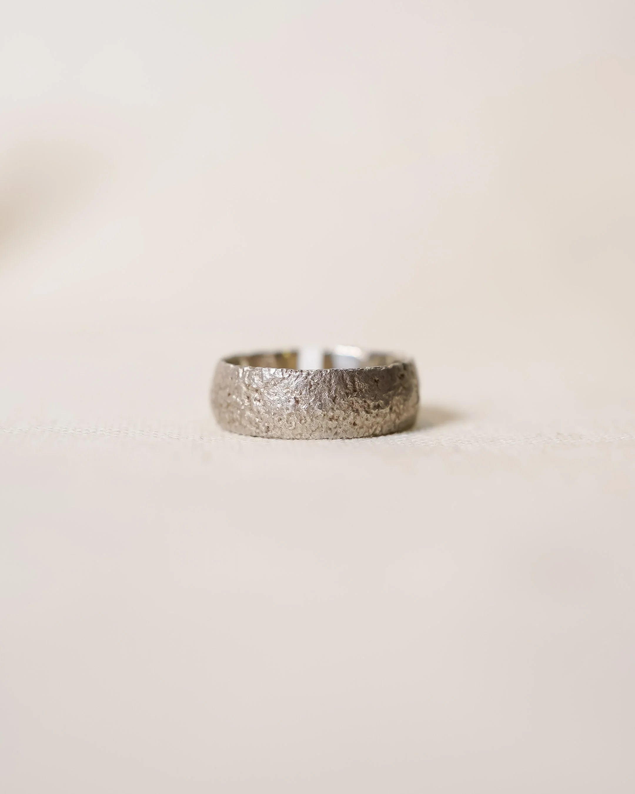 Handcrafted luxury ring with rugged textured finish on a neutral background