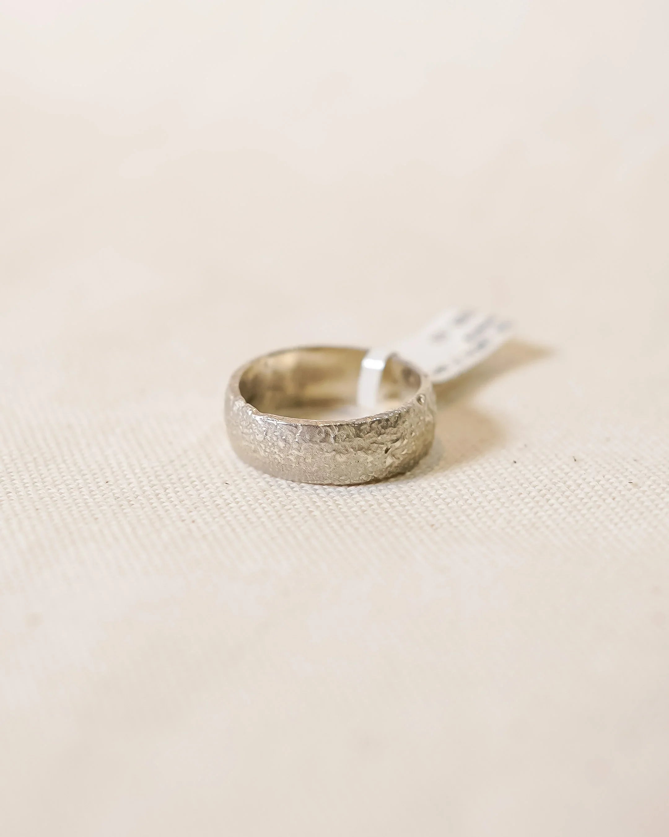 Handcrafted textured silver ring with organic design on neutral fabric background