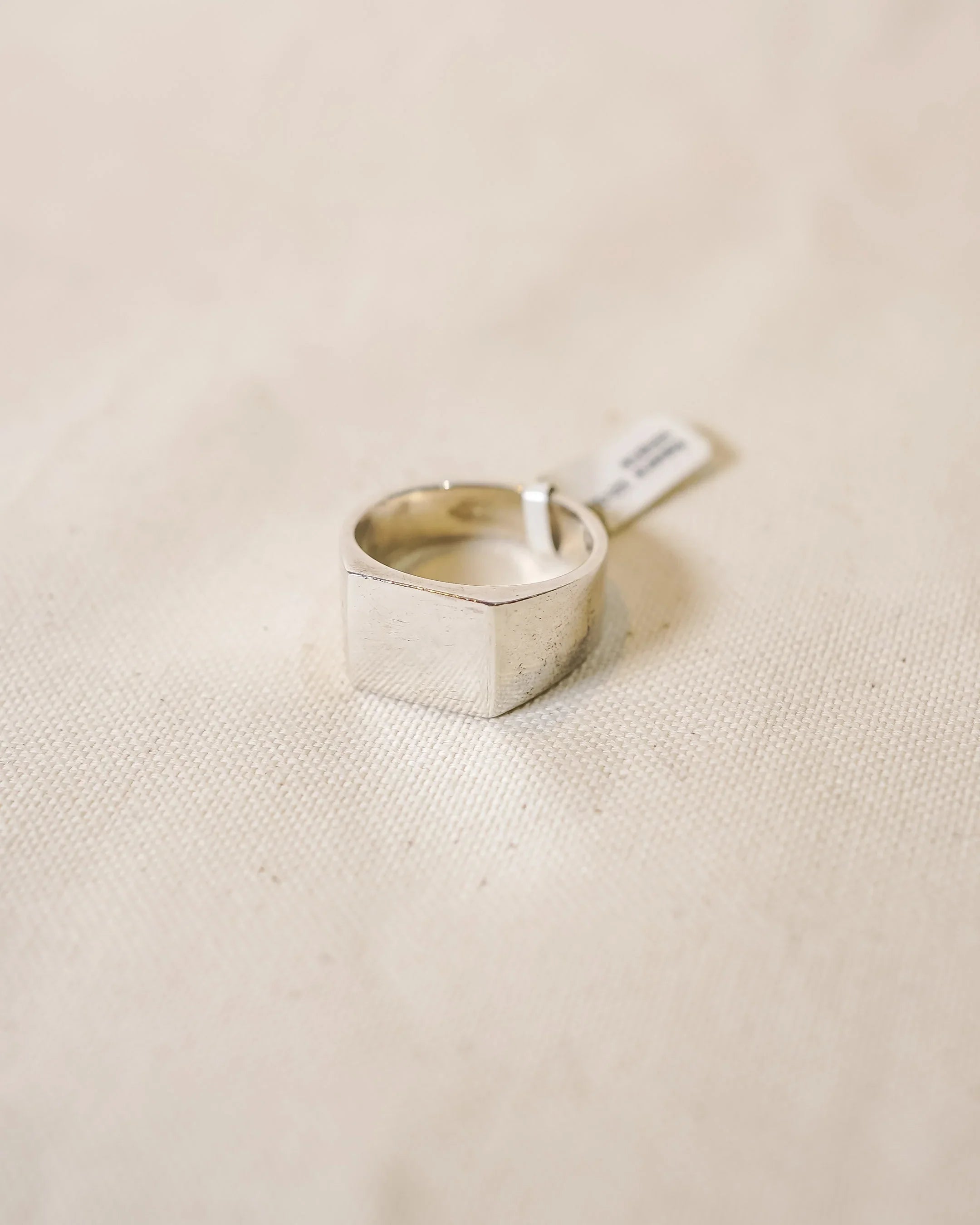 Handcrafted silver signet ring with a polished finish on a neutral fabric background