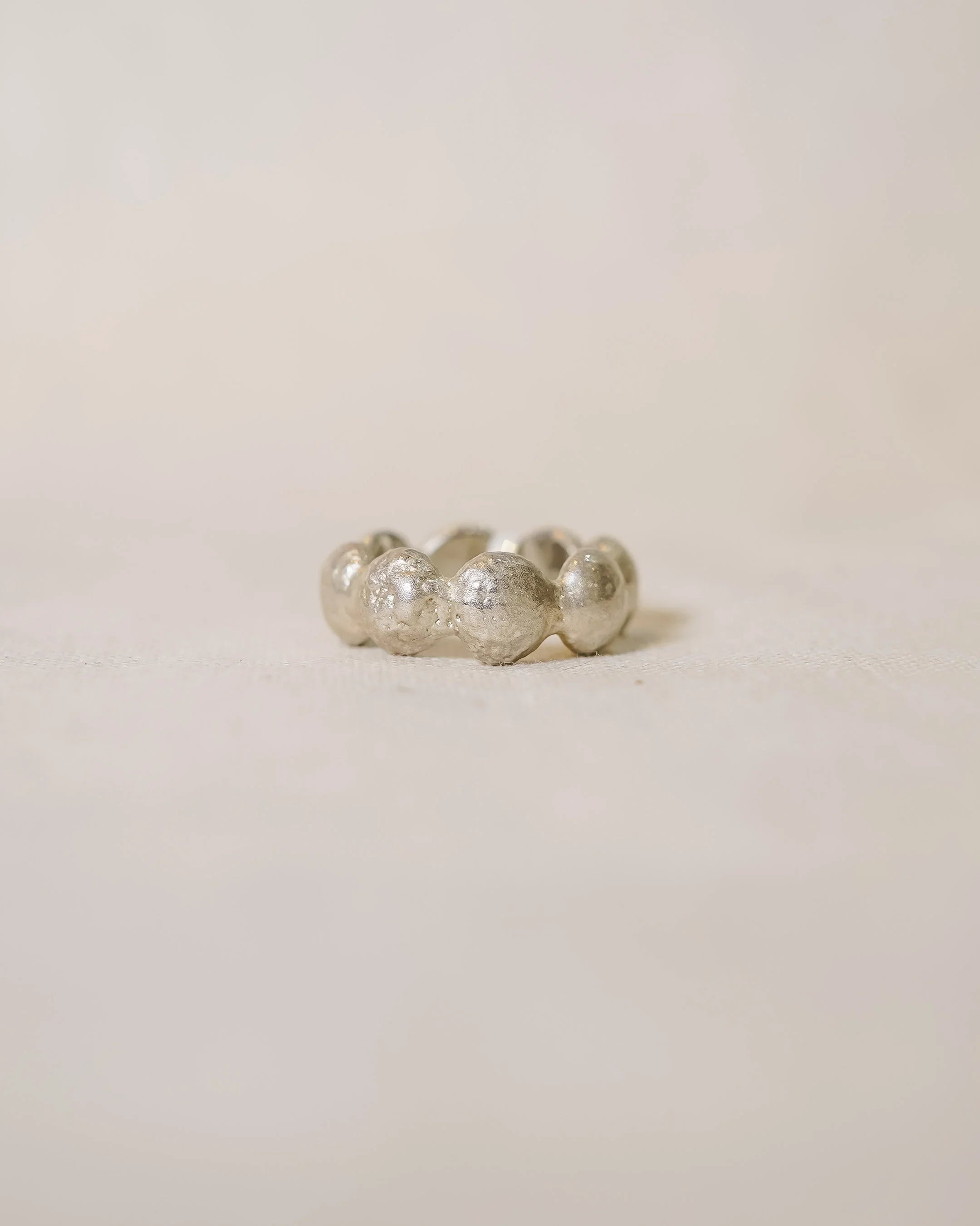 Handmade silver ring with organic, textured bubble design on a neutral background