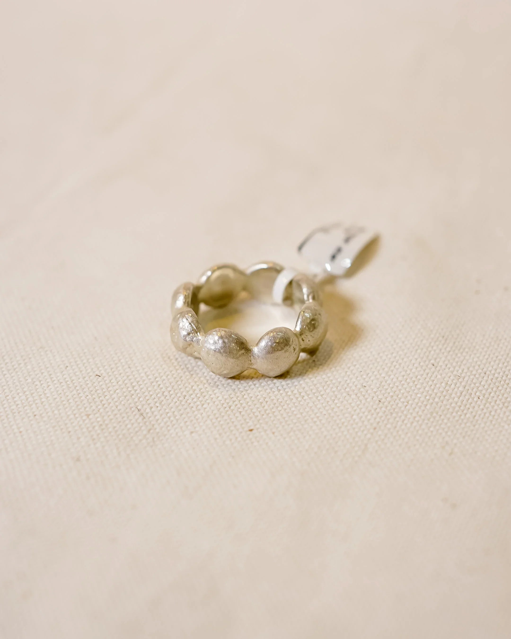 Handmade silver ring with organic, textured round shapes on neutral fabric background