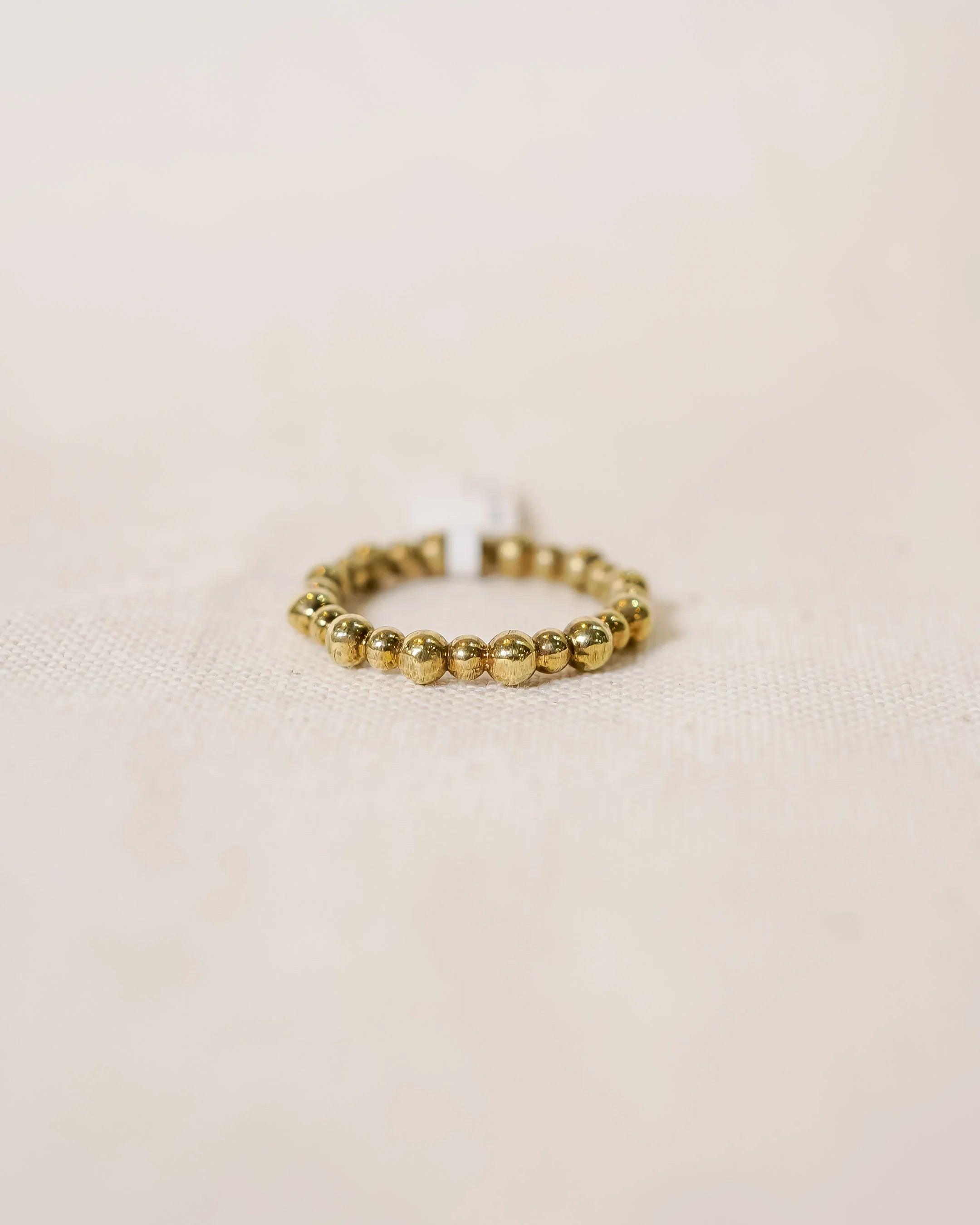 Handcrafted gold beaded ring with organic texture on a neutral fabric background