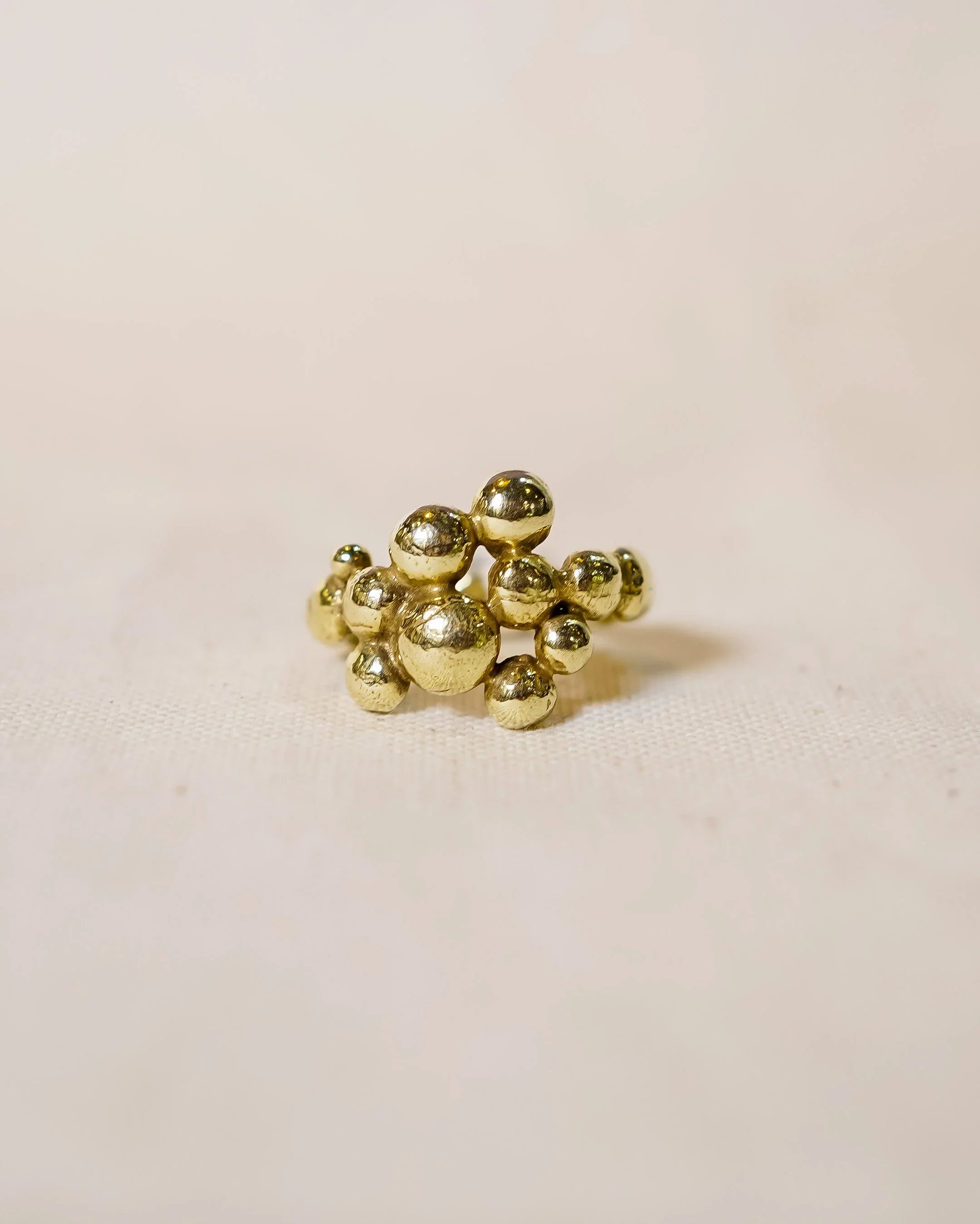 Handmade gold ring with organic clustered shapes and textured finish on neutral fabric background