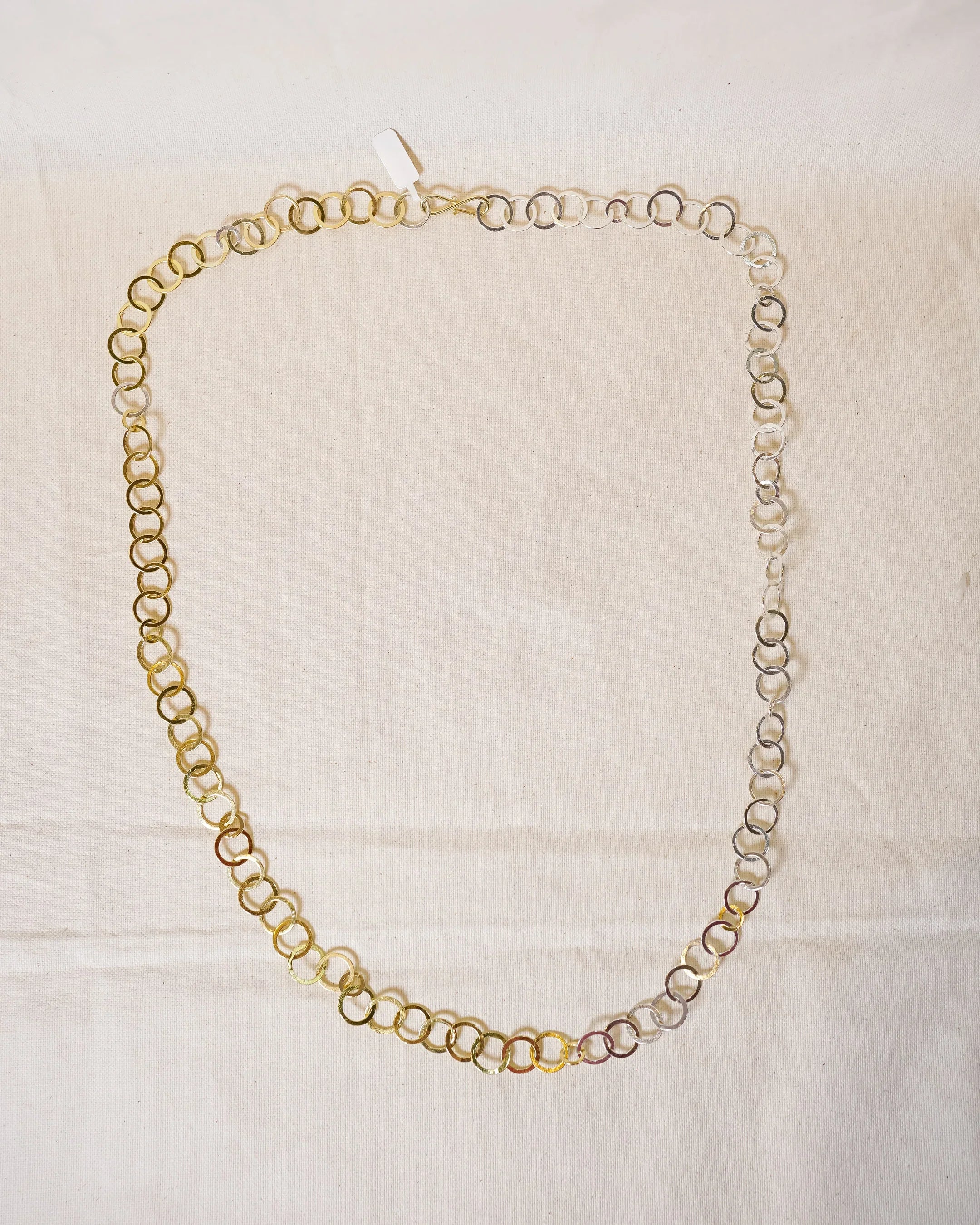 Handmade mixed metal circle link necklace with organic texture on cream fabric background