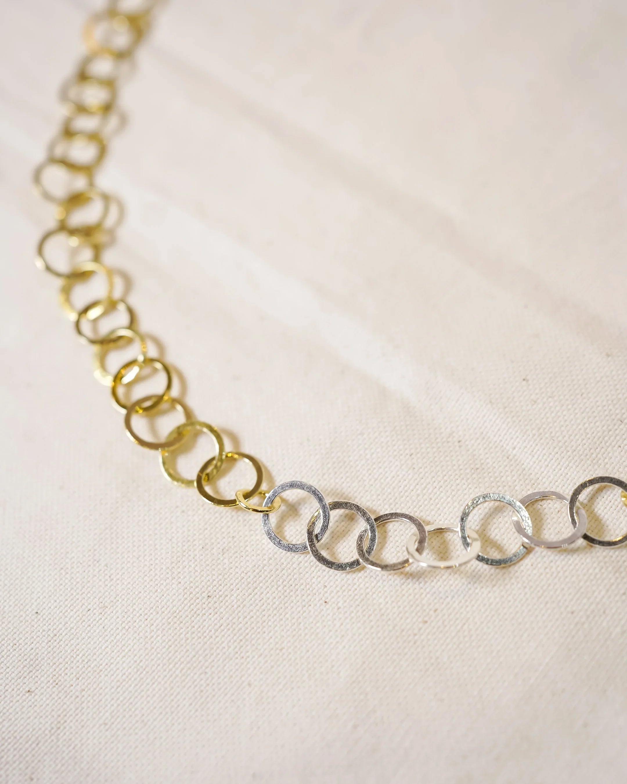 Handcrafted gold and silver linked chain necklace on cream fabric background