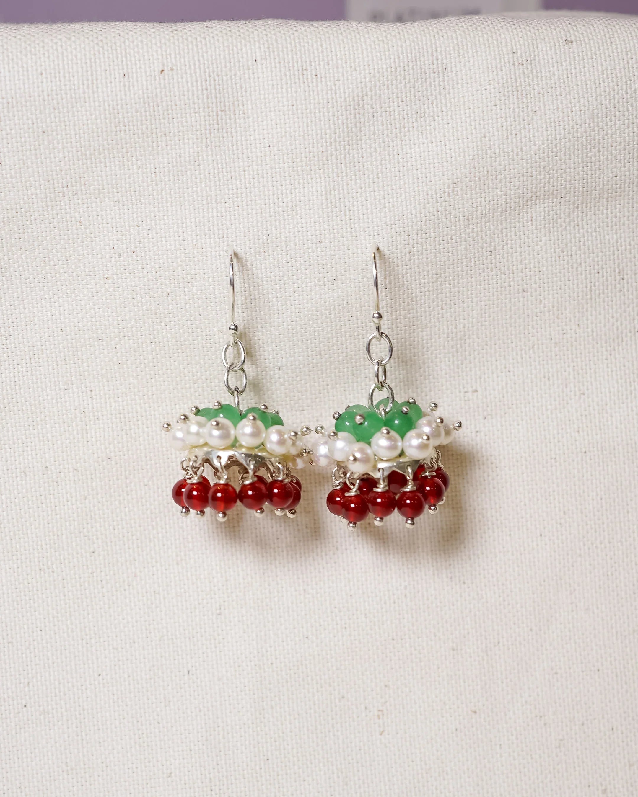 Handmade drop earrings with green, white, and red beads on a cream fabric background