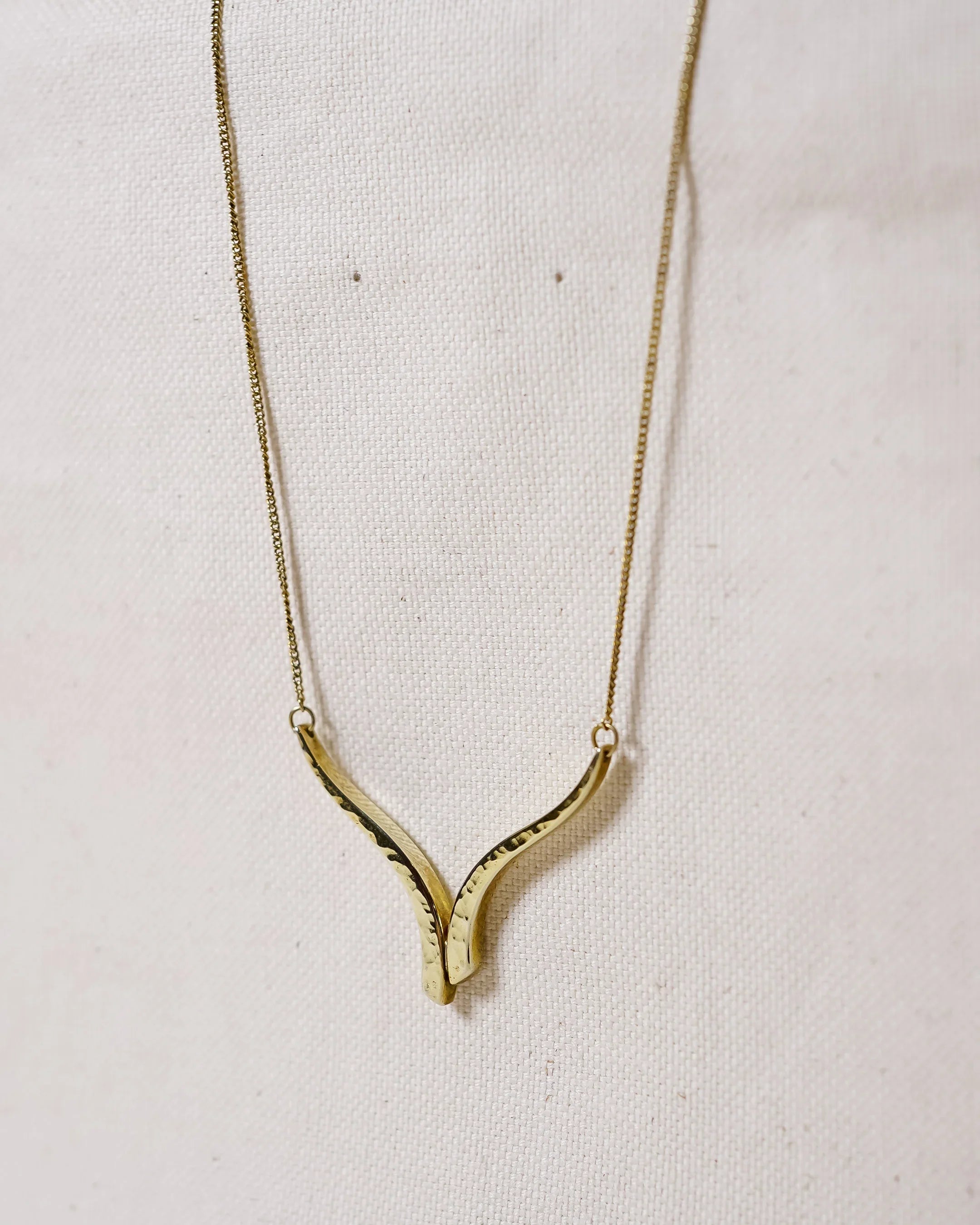 Handmade gold pendant necklace with organic, textured design on light fabric background