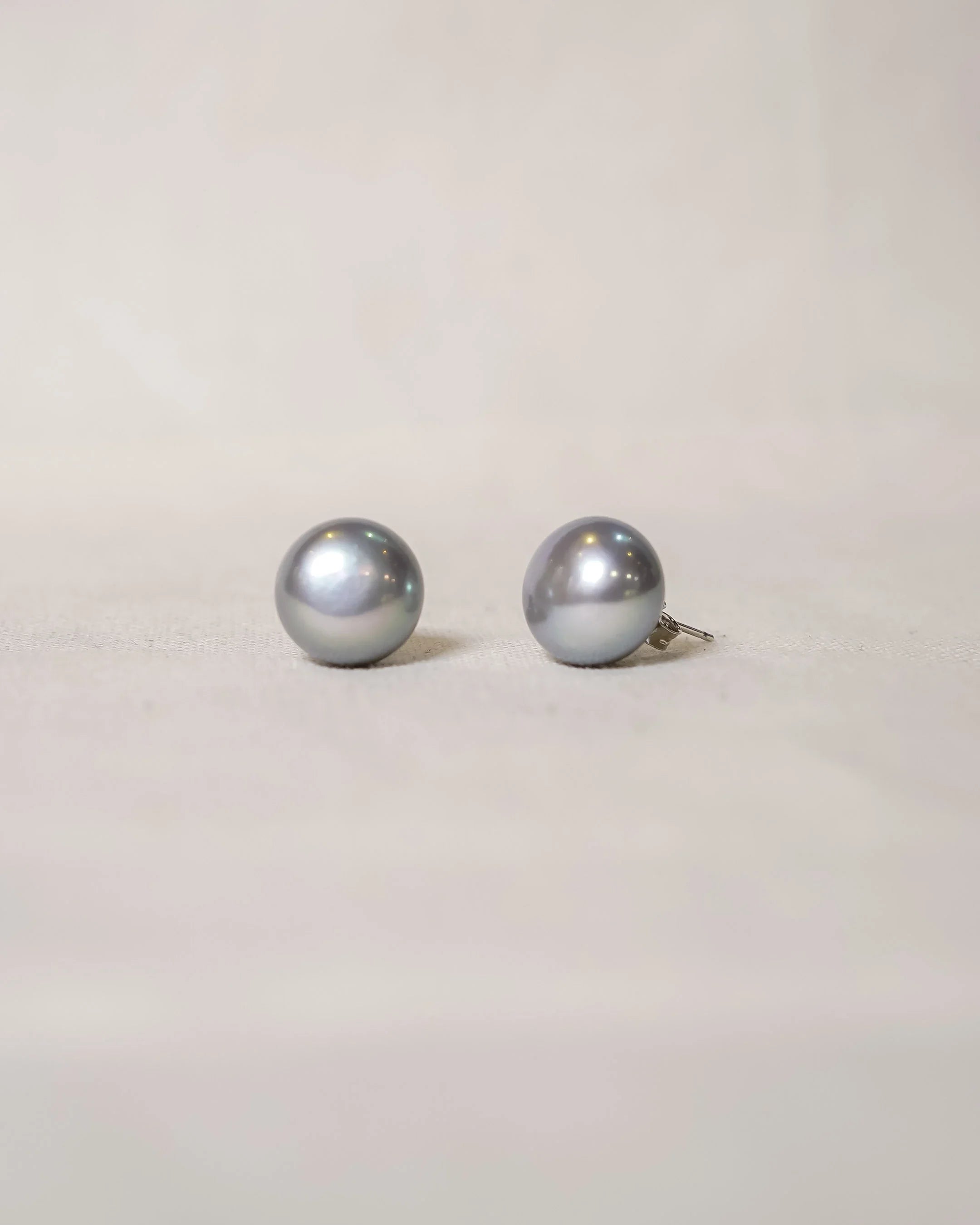 Pair of grey pearl stud earrings on light fabric background, handmade luxury jewellery