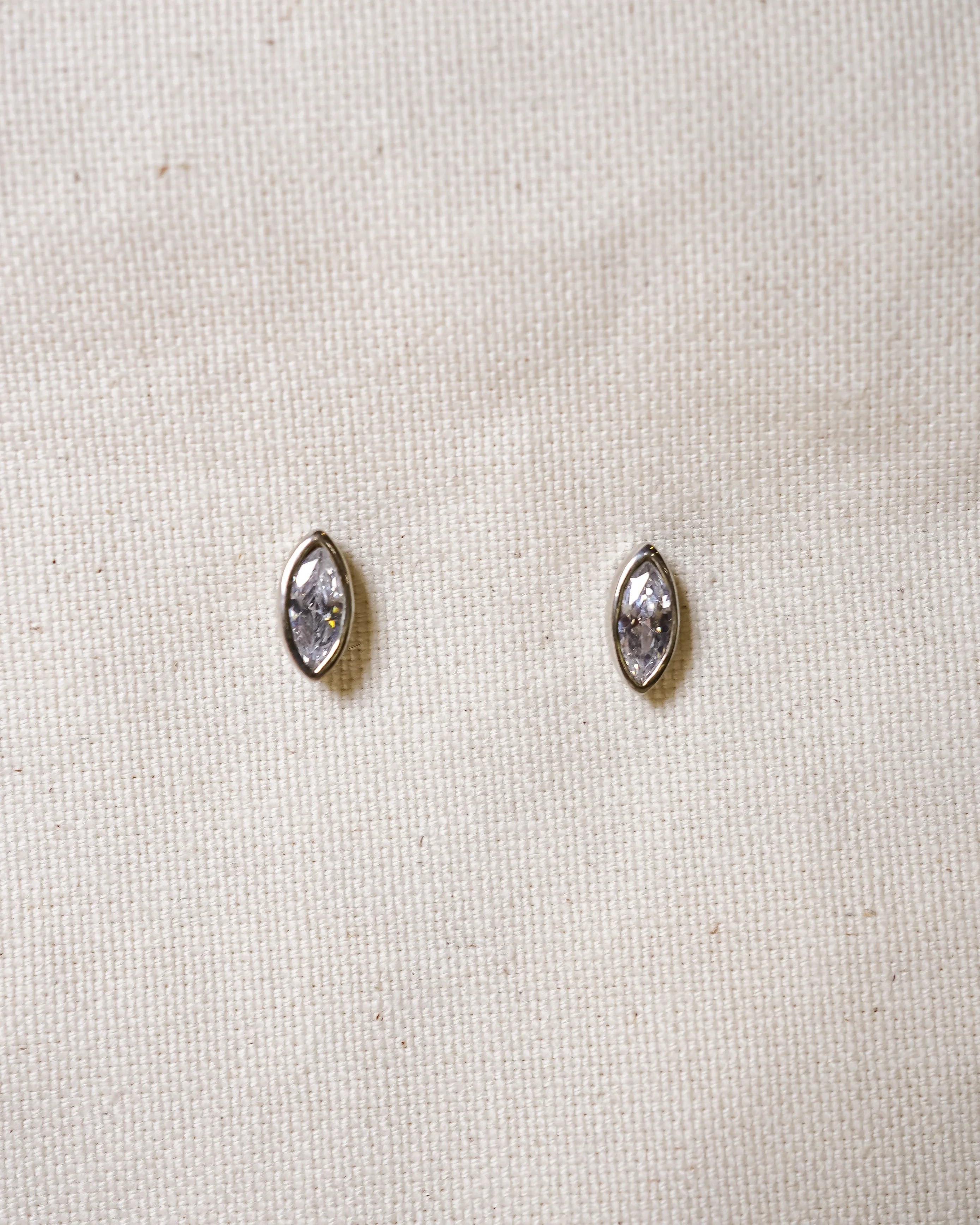 Marquise diamond stud earrings set in silver on textured fabric background