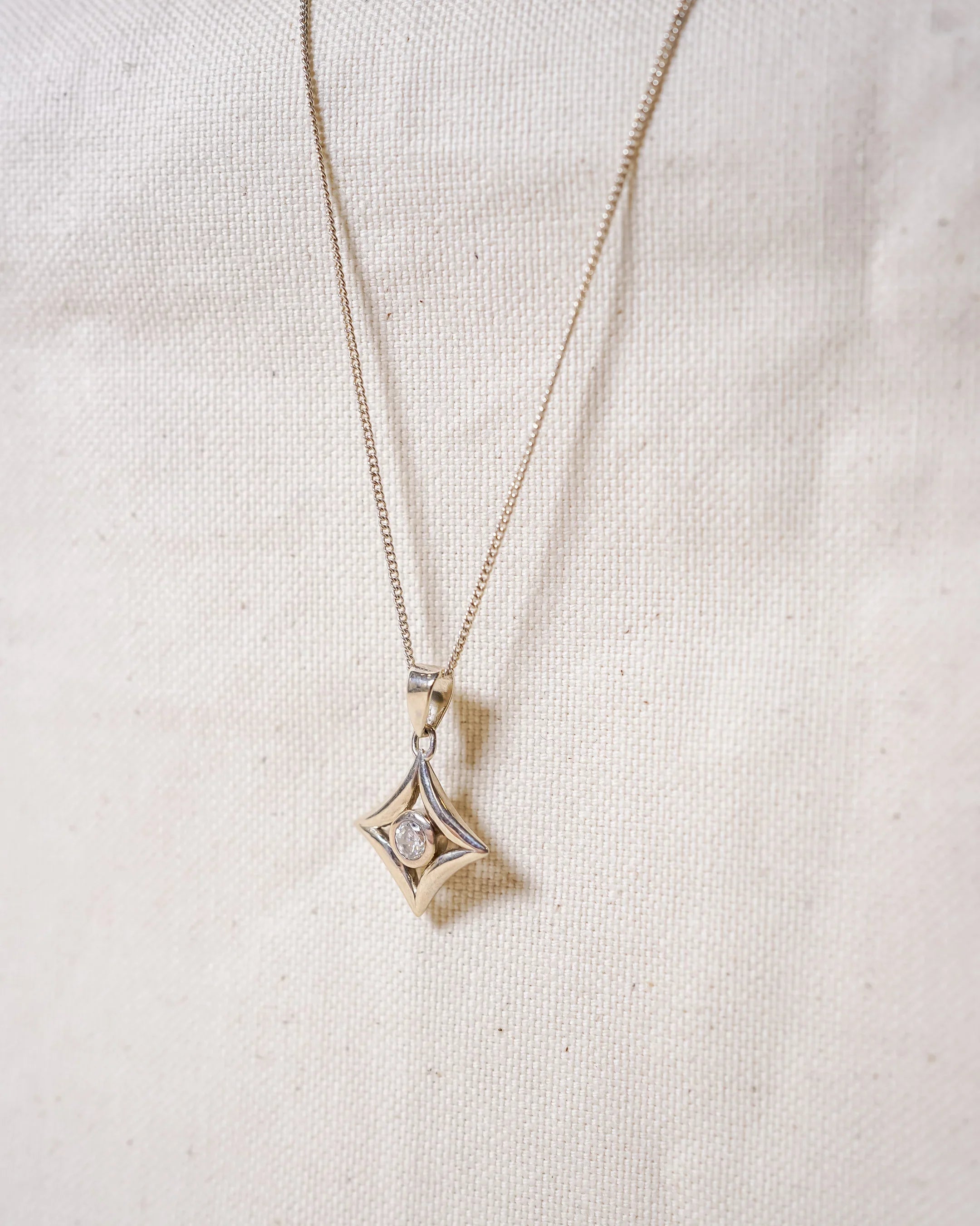 Handmade gold pendant necklace with diamond on textured fabric background