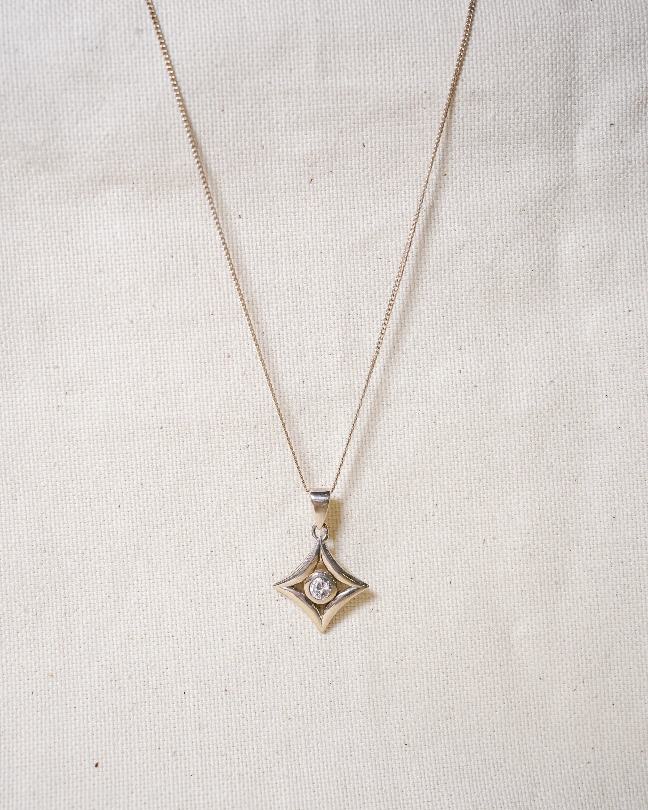 Handmade silver diamond pendant necklace with star-shaped design on textured beige background