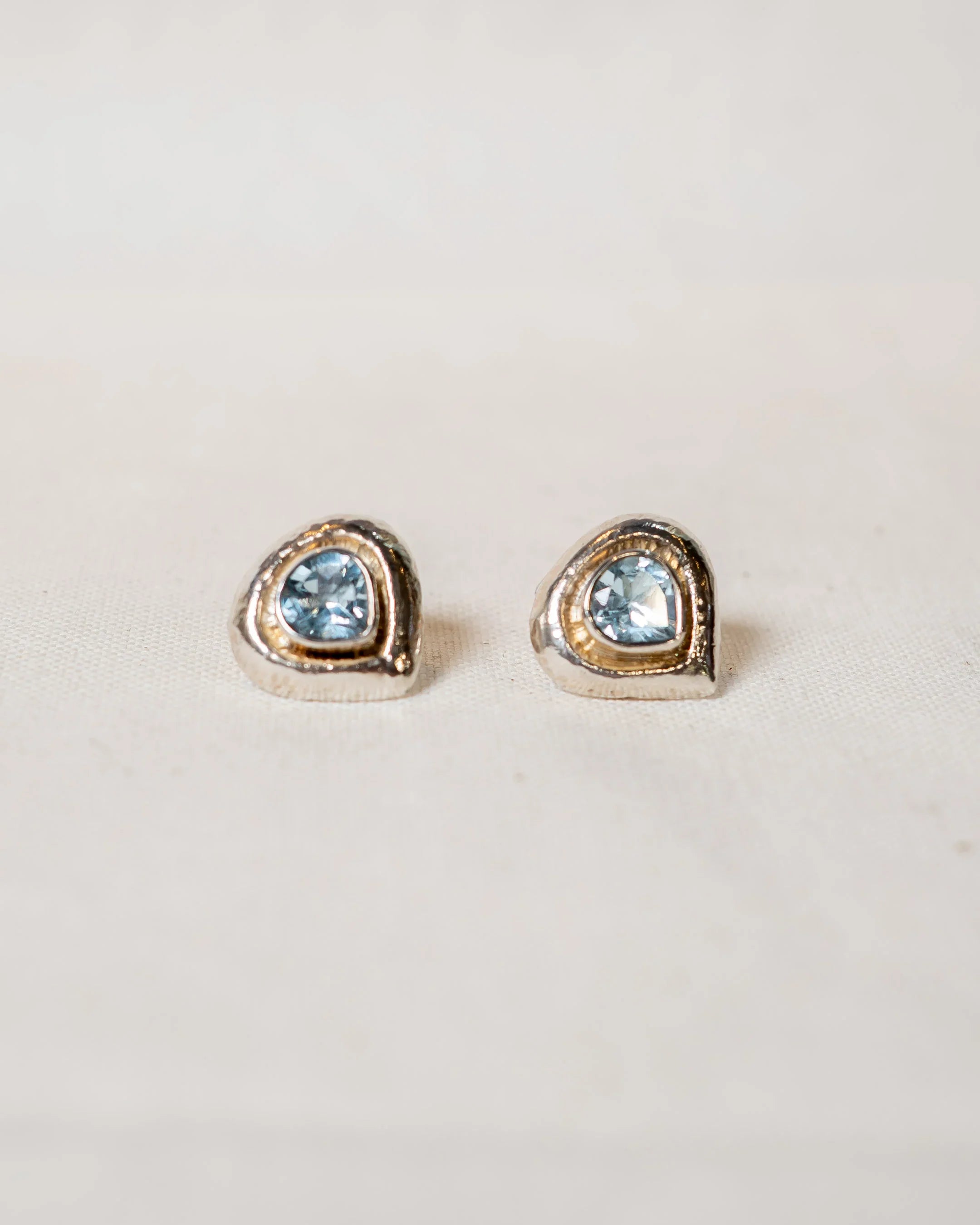Handcrafted stud earrings with blue gemstones set in organic gold and silver shapes on fabric