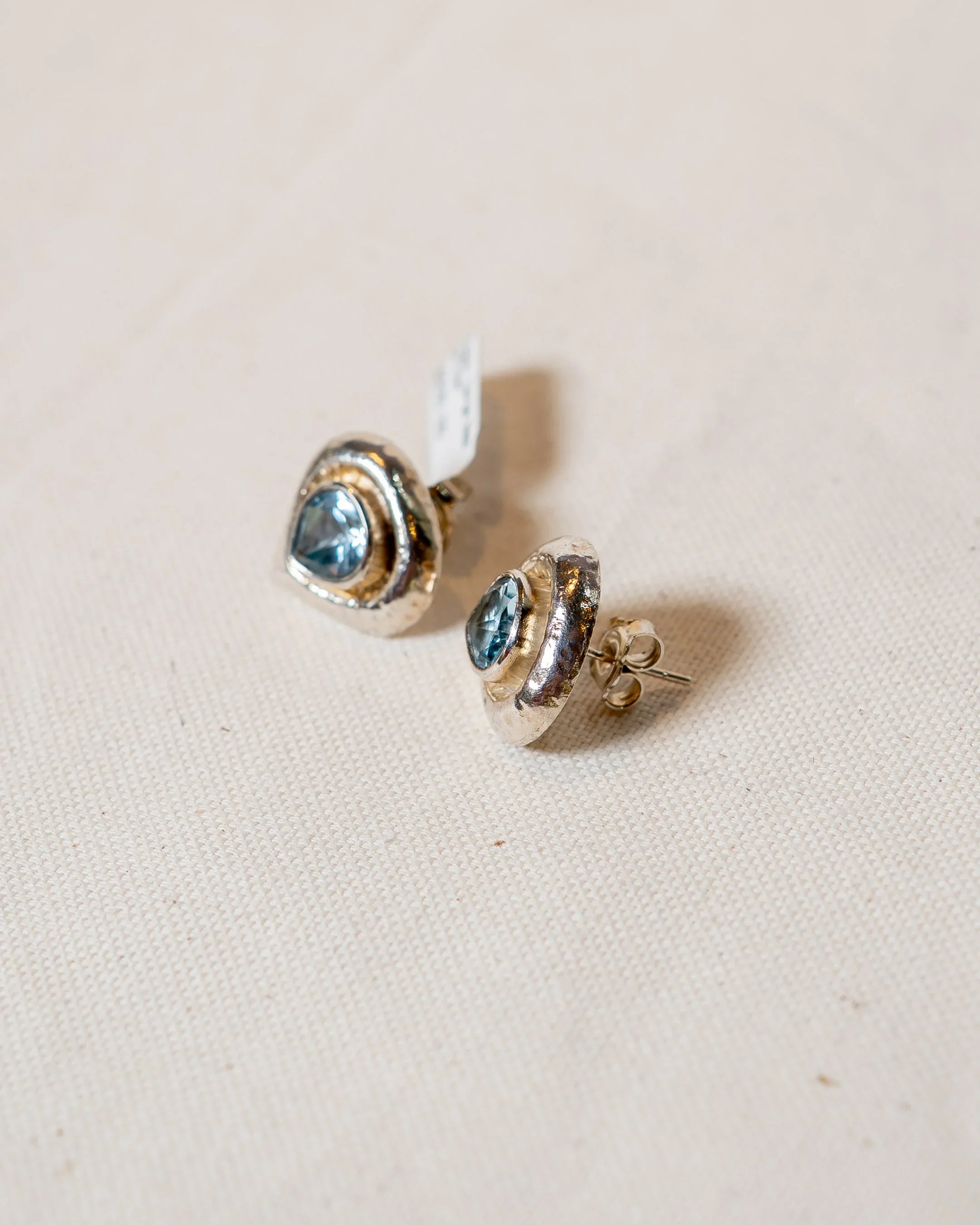 Handmade silver stud earrings with blue gemstones on a natural fabric background