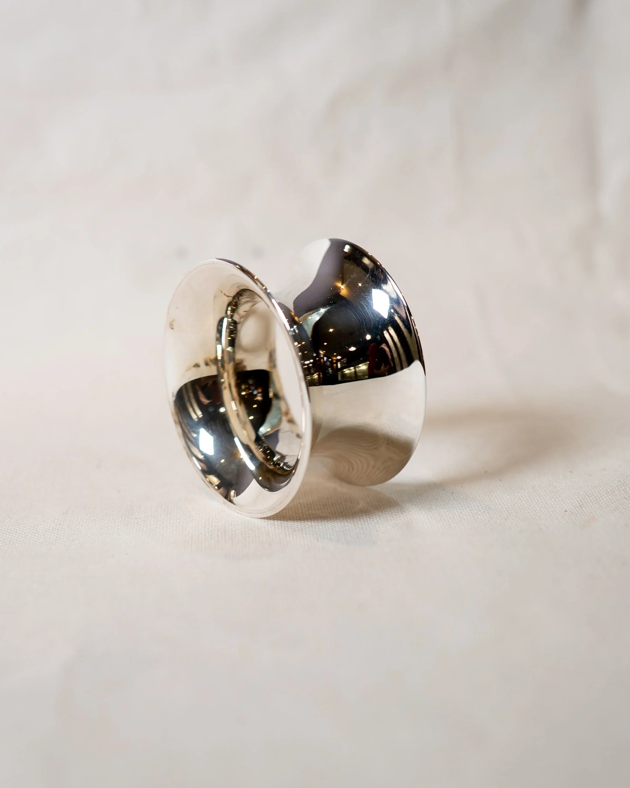 Handmade polished silver ring with organic sculpted shape on neutral fabric background