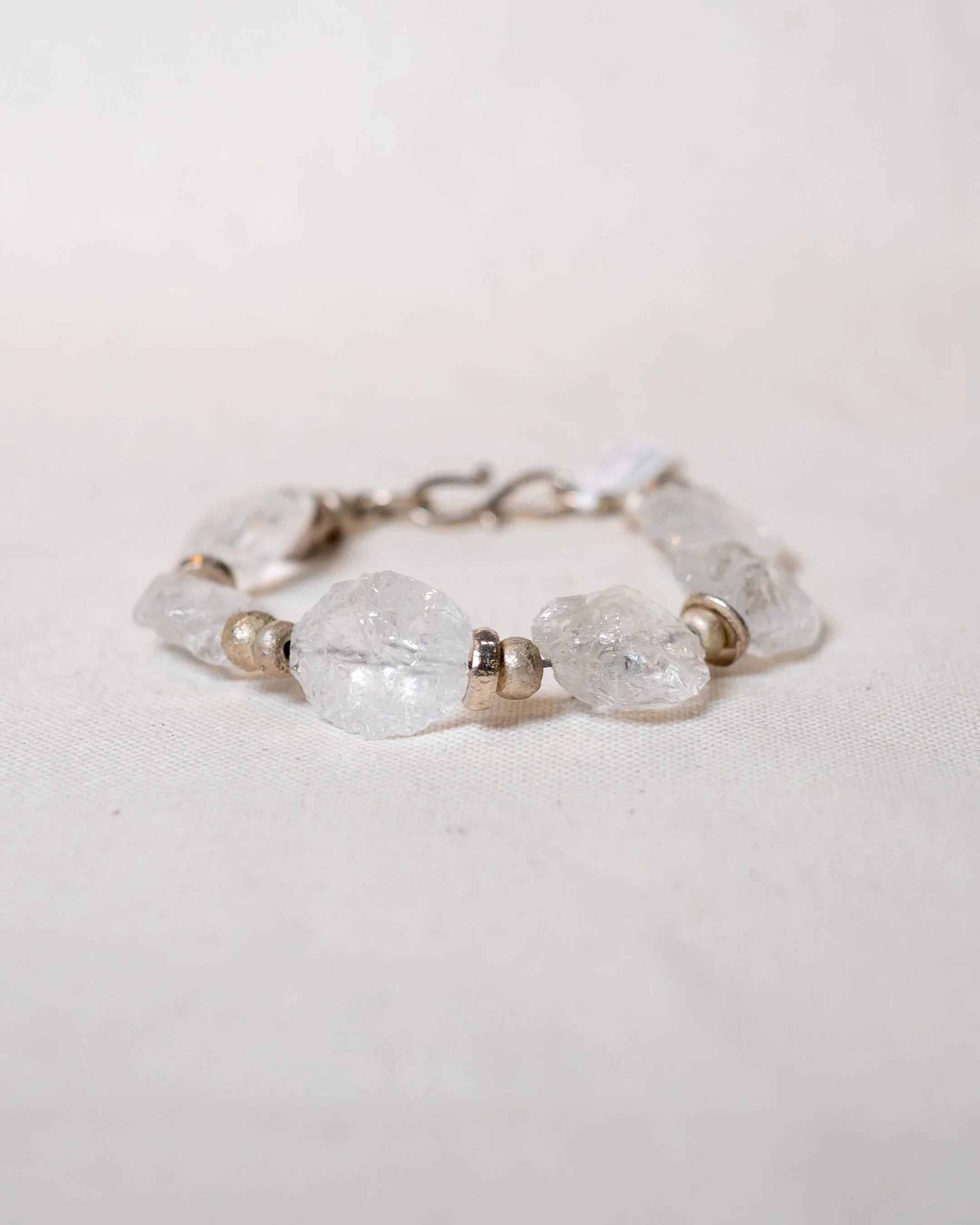 Handmade bracelet with raw quartz gemstones and silver beads on a neutral fabric background