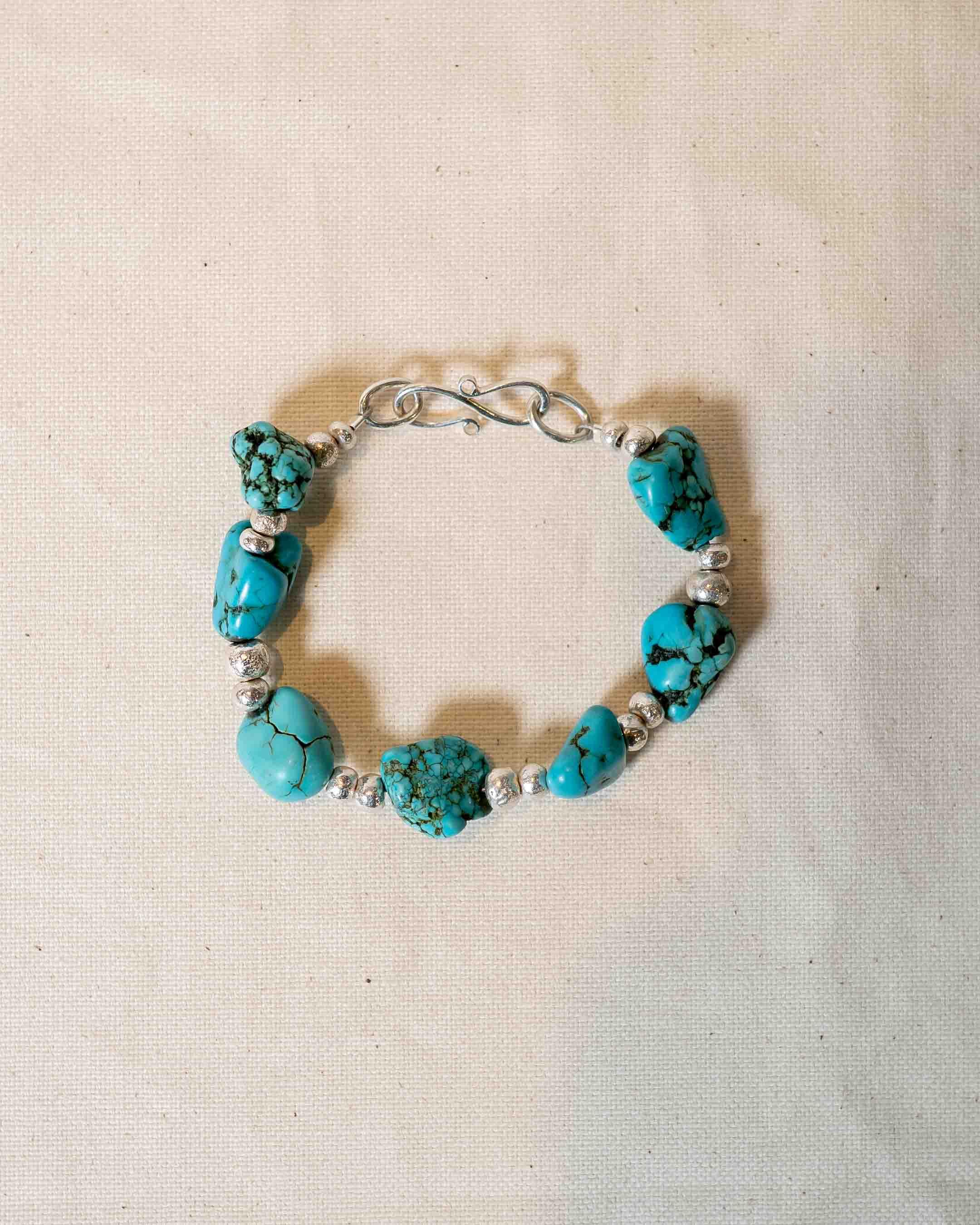 Handmade silver and turquoise stone bracelet with organic shapes on a neutral fabric background