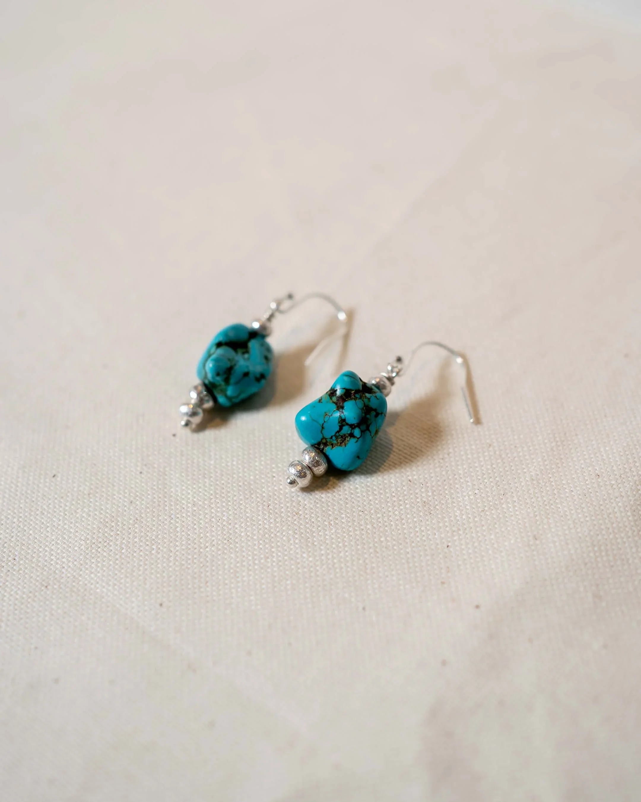 Handmade silver drop earrings with blue turquoise stones on a neutral fabric background