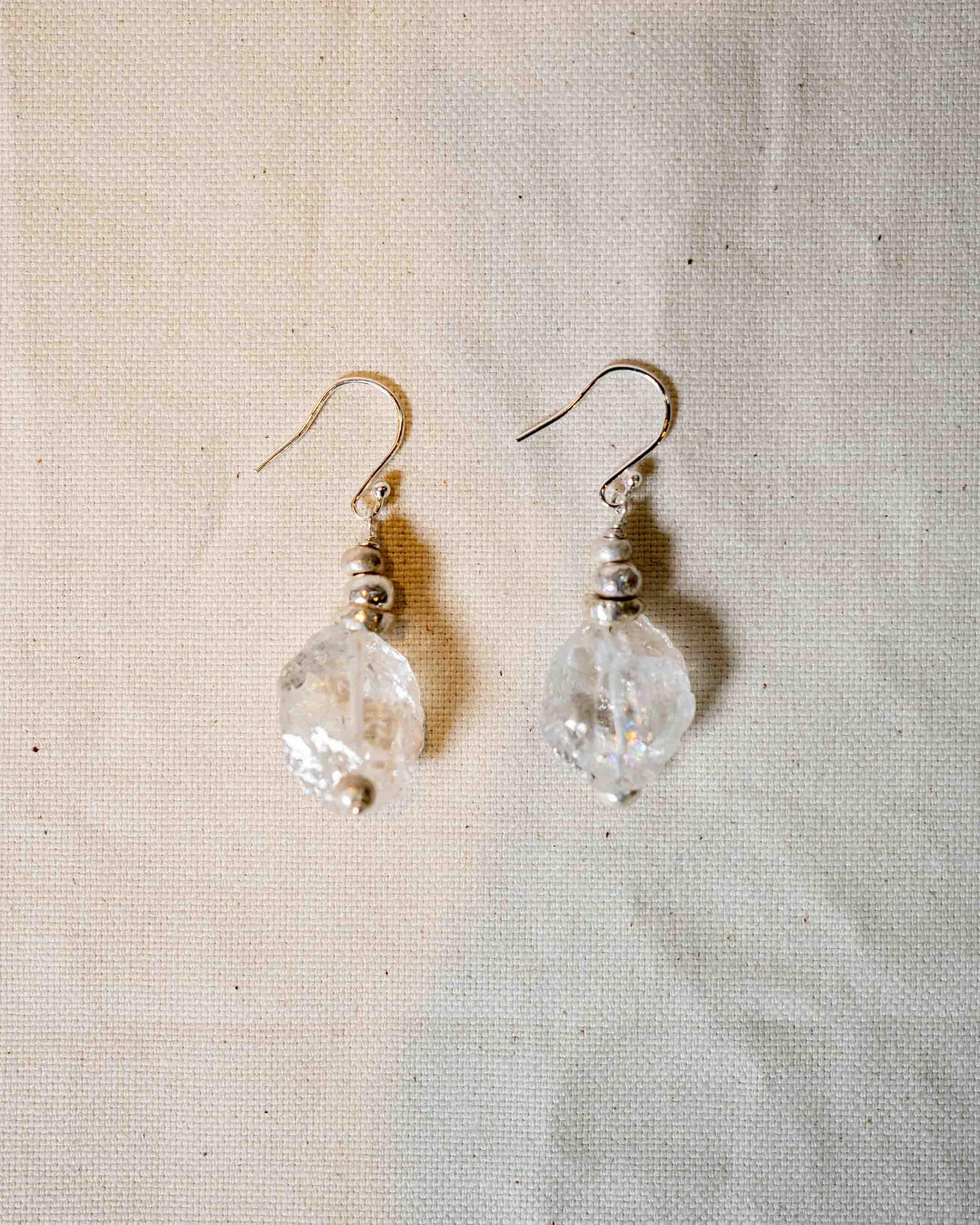 Handmade silver and crystal drop earrings with organic texture on a neutral fabric background
