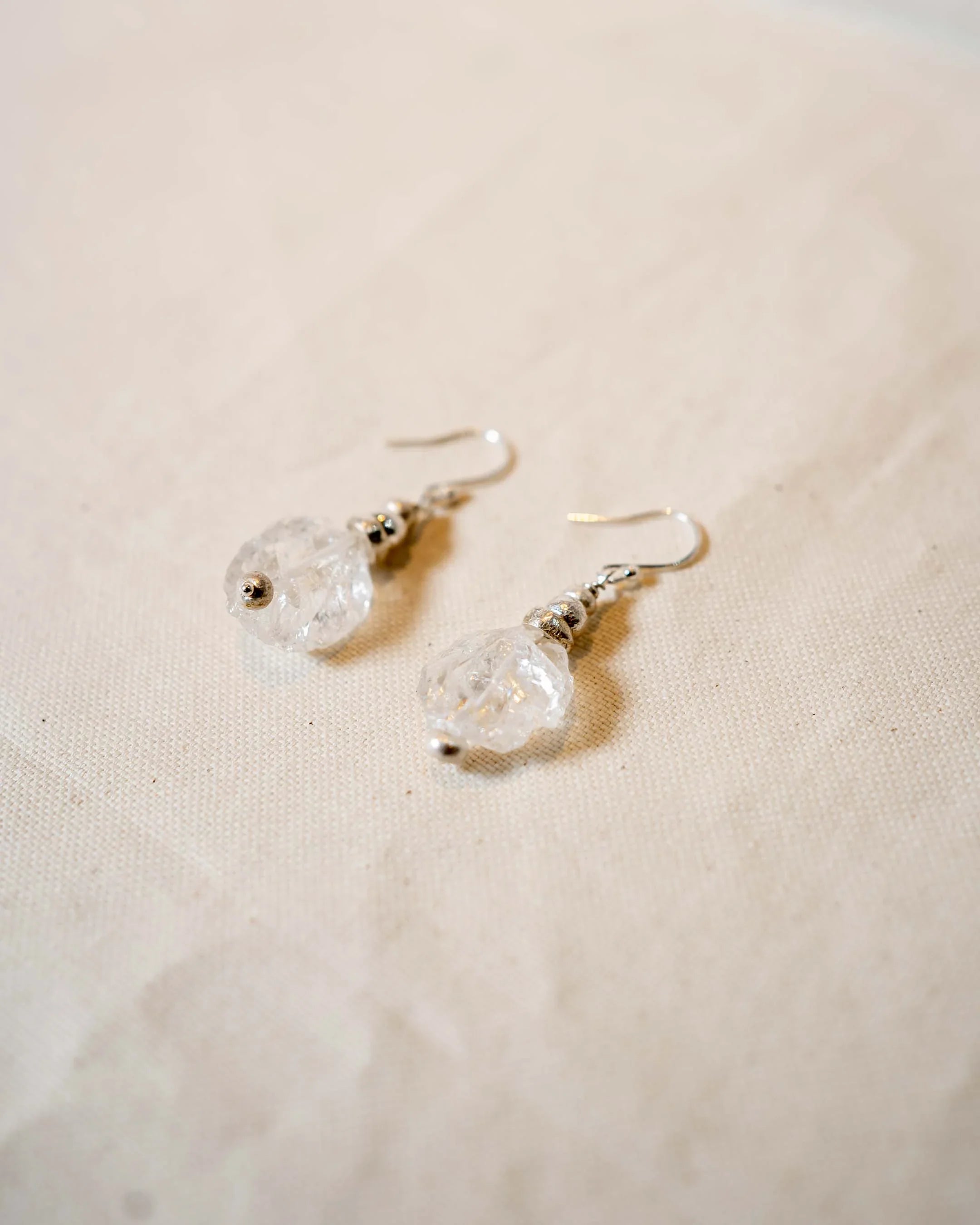 Handmade silver drop earrings with clear textured gemstone beads on neutral fabric