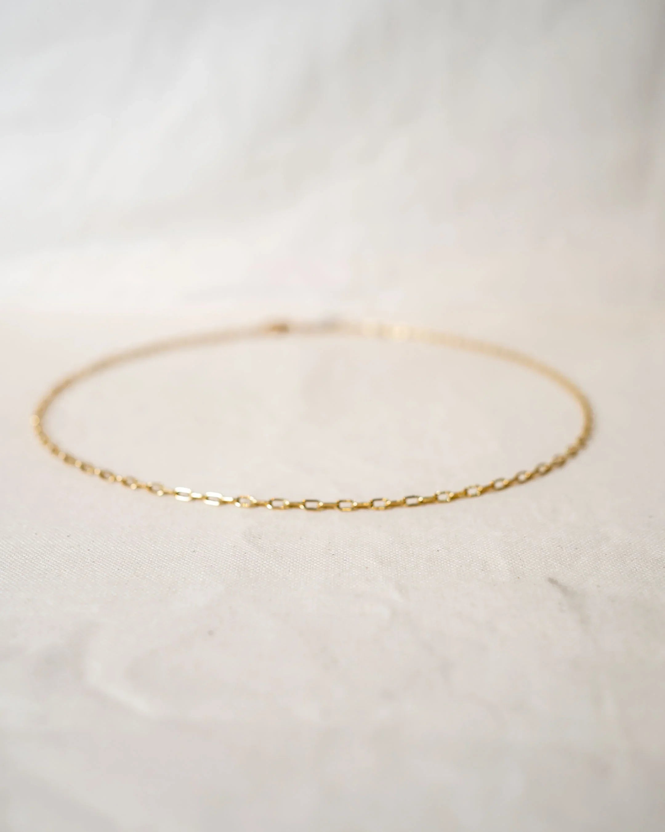 Delicate gold chain necklace with handmade links on a soft fabric background