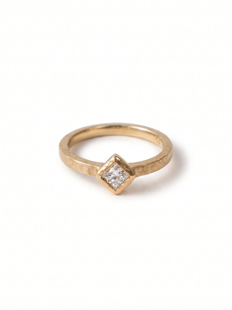 Gold engagement ring with a hammered texture and a square princess-cut diamond in a bezel setting.