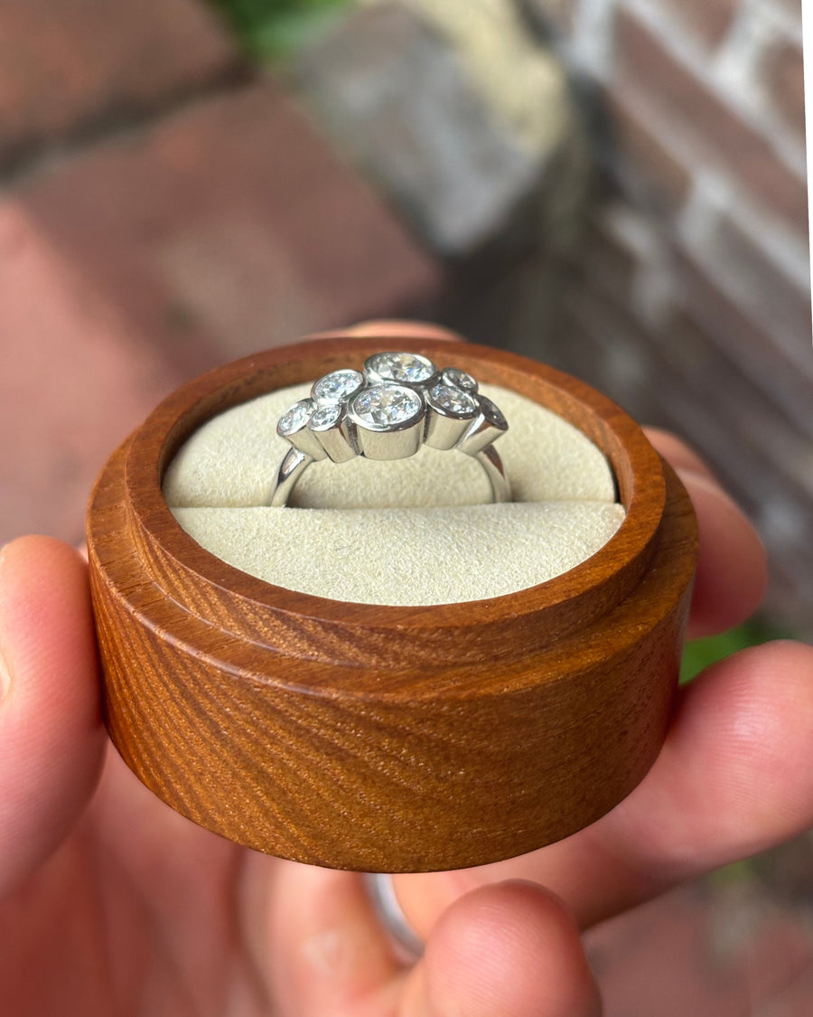 White gold engagement ring with a cluster of round diamonds in a bubble setting inside a wooden box.