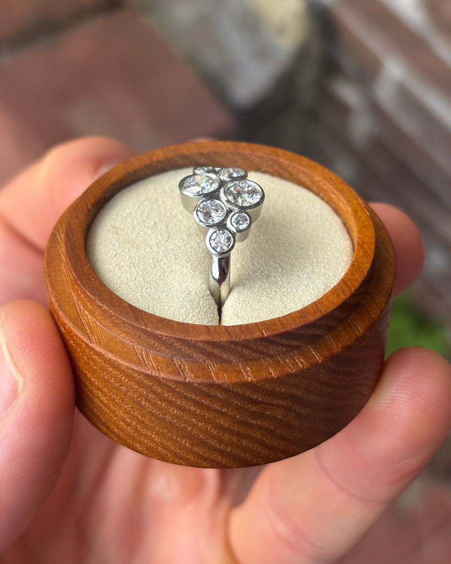 Silver engagement ring with a cluster of round diamonds in a bubble design inside a wooden box.