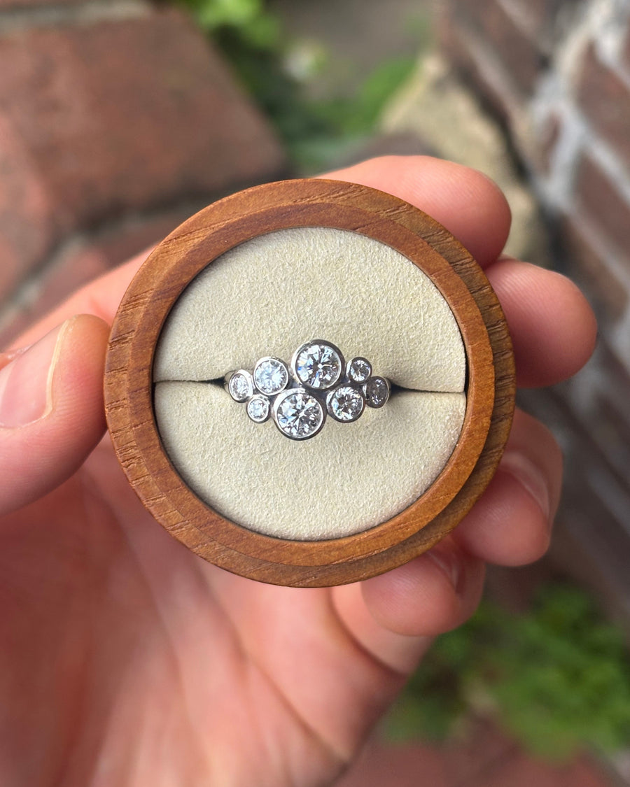 Silver cluster engagement ring with round diamonds in a bubble setting inside a wooden ring box.