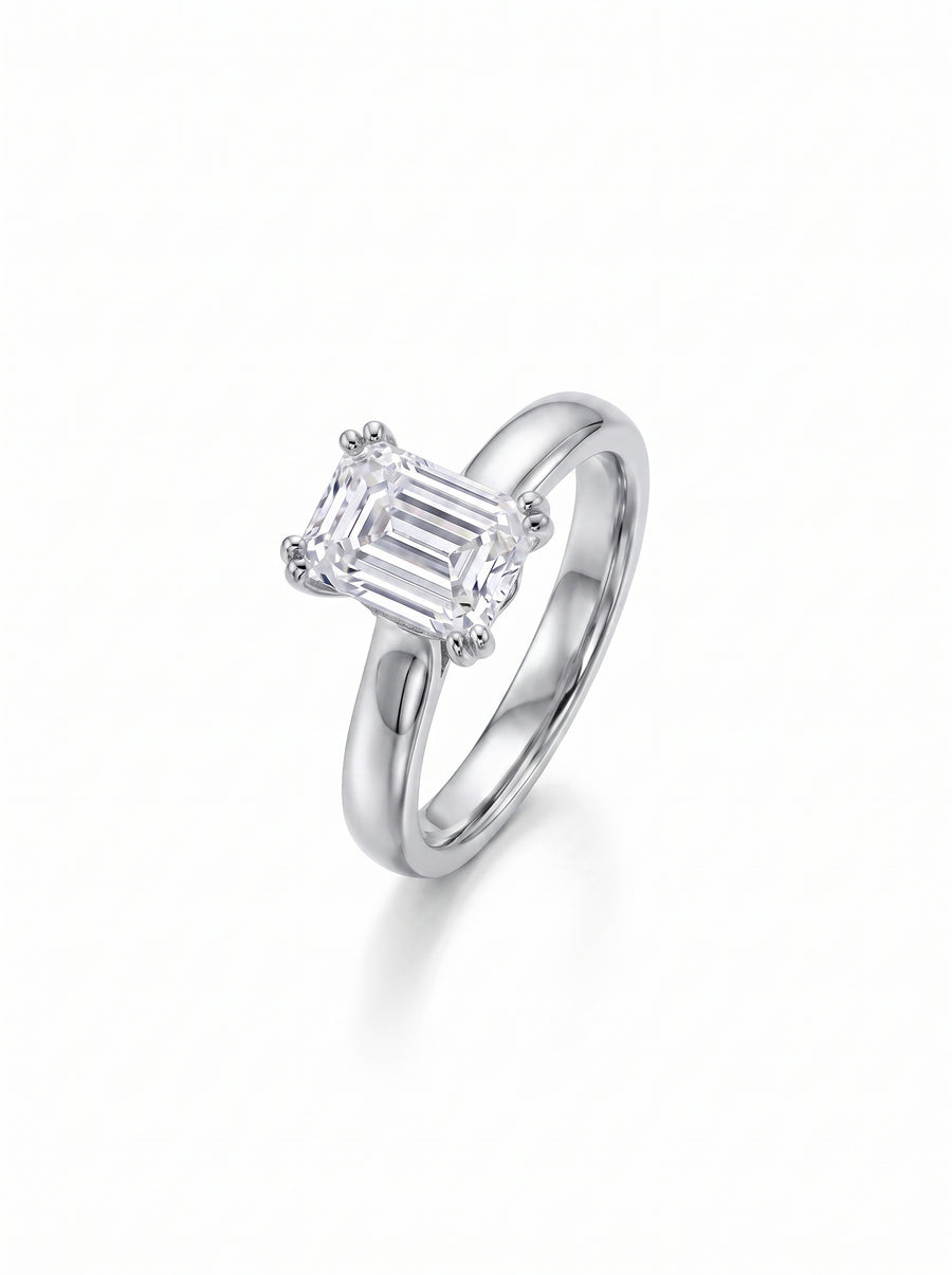 Emerald-cut diamond solitaire engagement ring set in a polished silver-toned metal cathedral band.