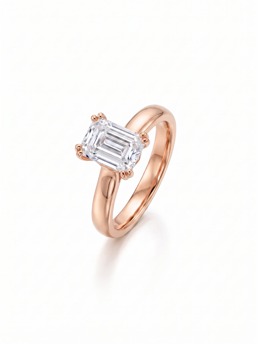 Emerald-cut diamond solitaire engagement ring set on a polished rose gold cathedral band.