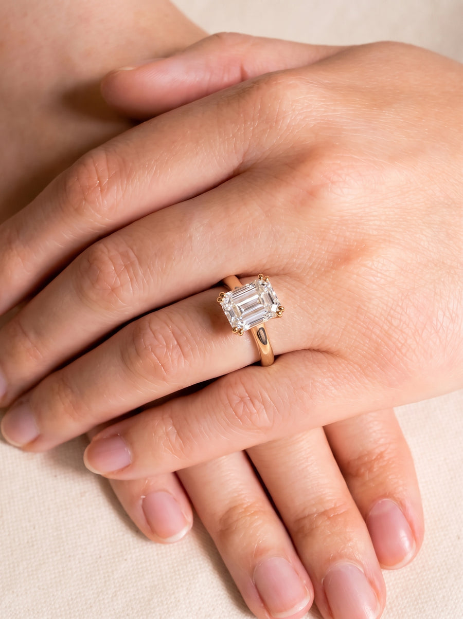Emerald-cut diamond solitaire engagement ring with a gold cathedral setting worn on a finger.