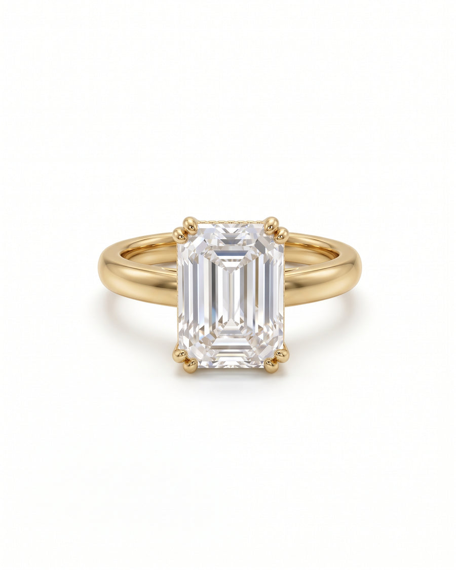 Emerald-cut solitaire engagement ring with a clear gemstone set in a polished yellow gold cathedral band.