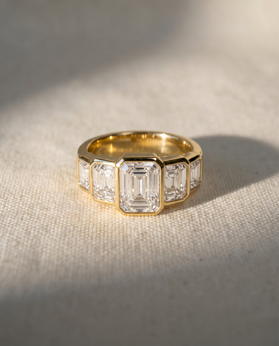 Gold ring featuring five bezel-set emerald cut diamonds in an art deco style.