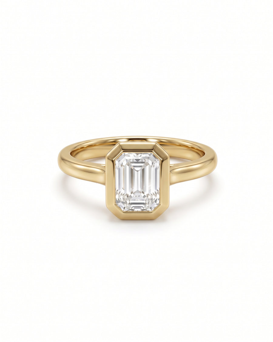 Emerald cut diamond engagement ring in a gold bezel setting with a cathedral band.