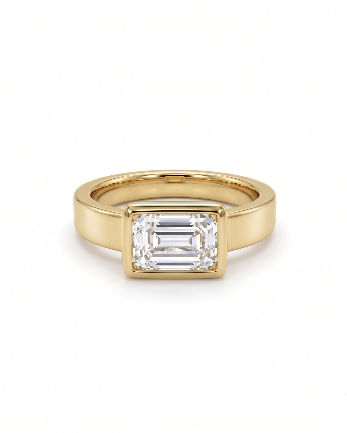 Emerald cut diamond engagement ring in a yellow gold bezel setting on a white background.
