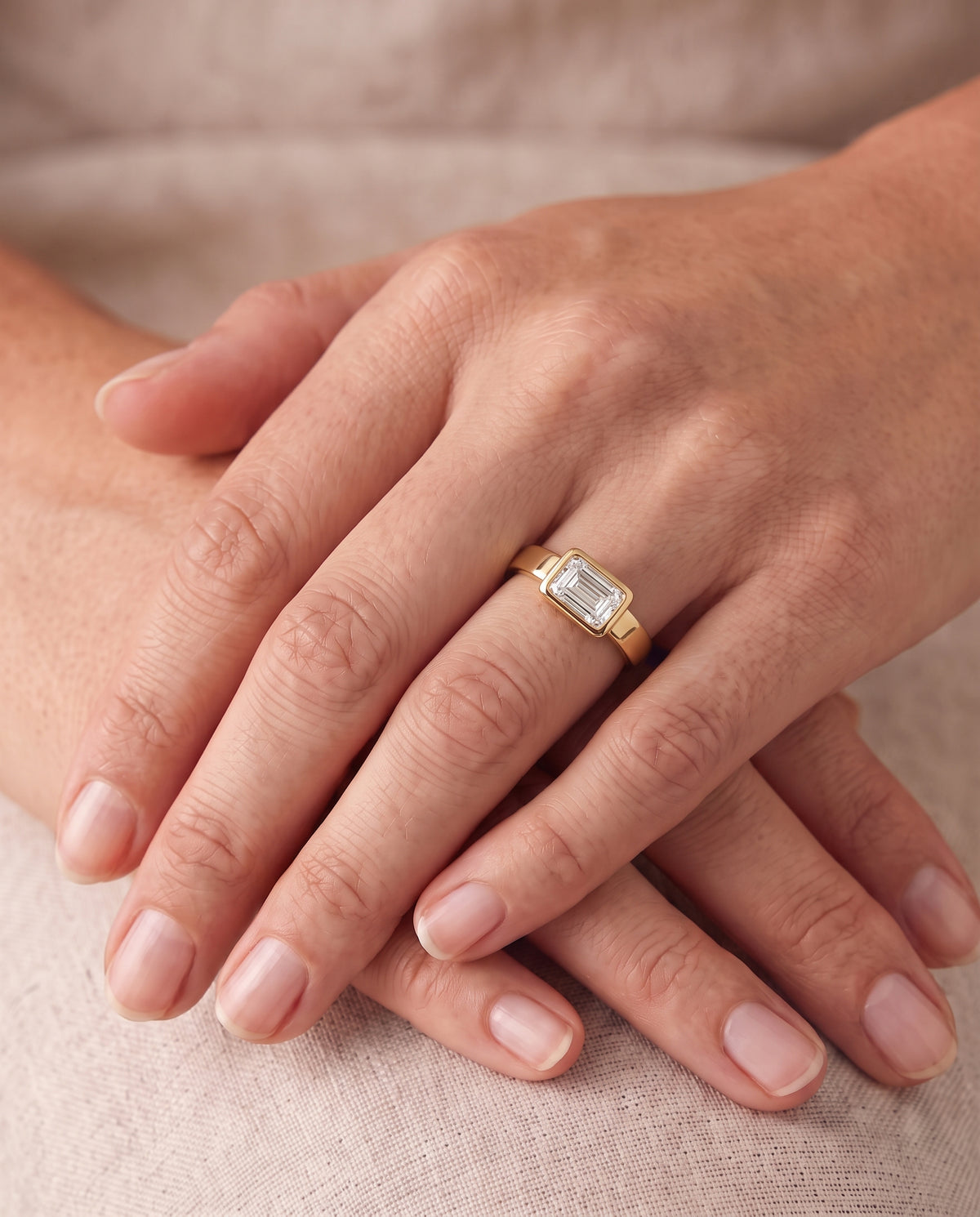 Emerald cut diamond engagement ring in a gold bezel setting worn on a finger.