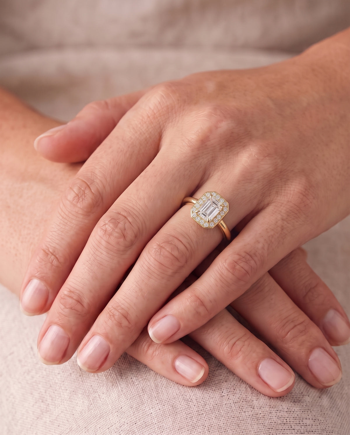 Emerald-cut diamond engagement ring with a diamond halo on a gold band worn on a finger.