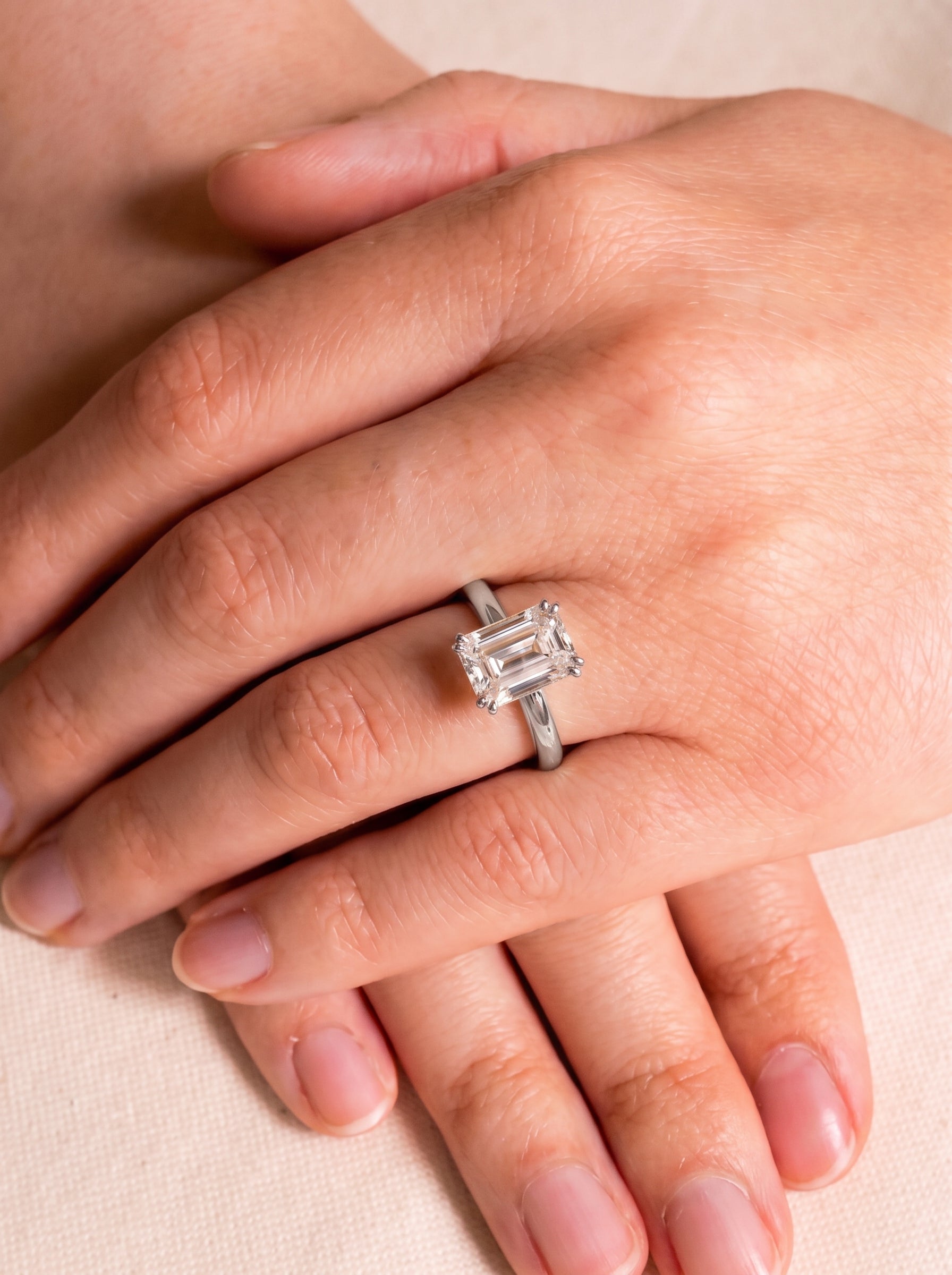 Emerald cut diamond engagement ring with a hidden halo on a silver band worn on a finger.