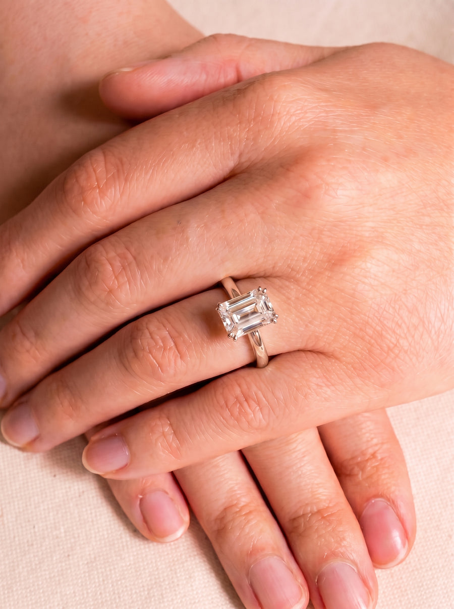 Emerald cut diamond engagement ring with a hidden halo on a silver band worn on a finger.