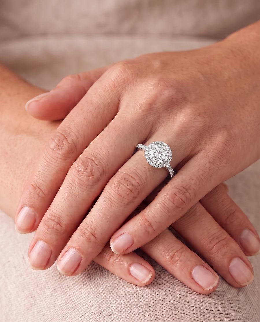 Round diamond cluster engagement ring with a pavé band set in white gold on a woman's finger.