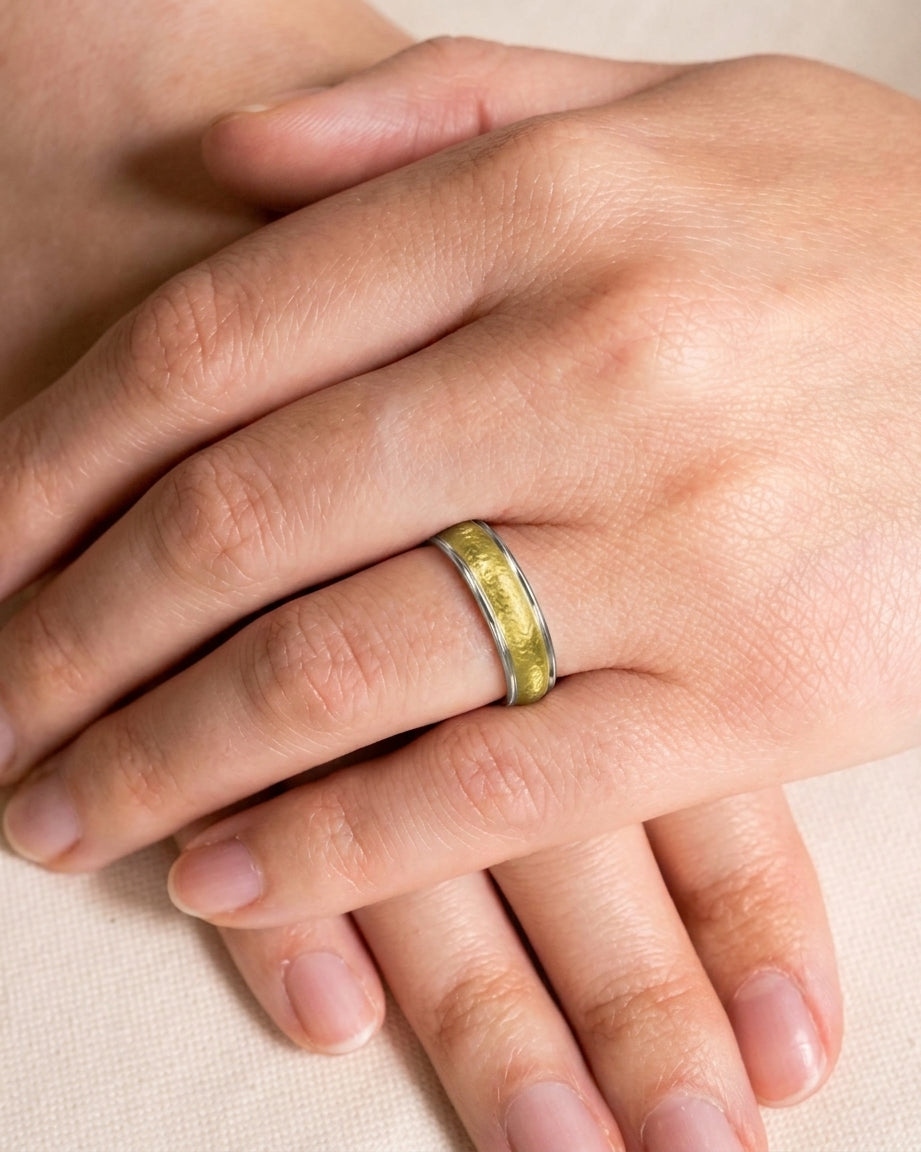 Two-tone wedding band with a textured matte gold center and smooth silver edges worn on a finger.