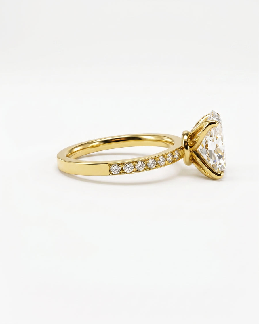 A yellow gold ring featuring a large triangular clear gemstone in a prong setting, with a pavé band accented by small round diamonds, shown on a clean white background.
