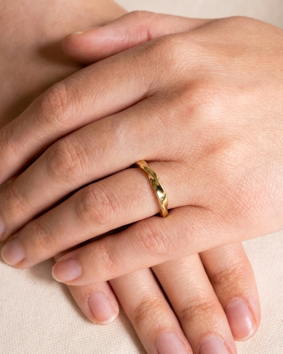 A polished gold ring with a subtle, twisted band design worn on a finger.