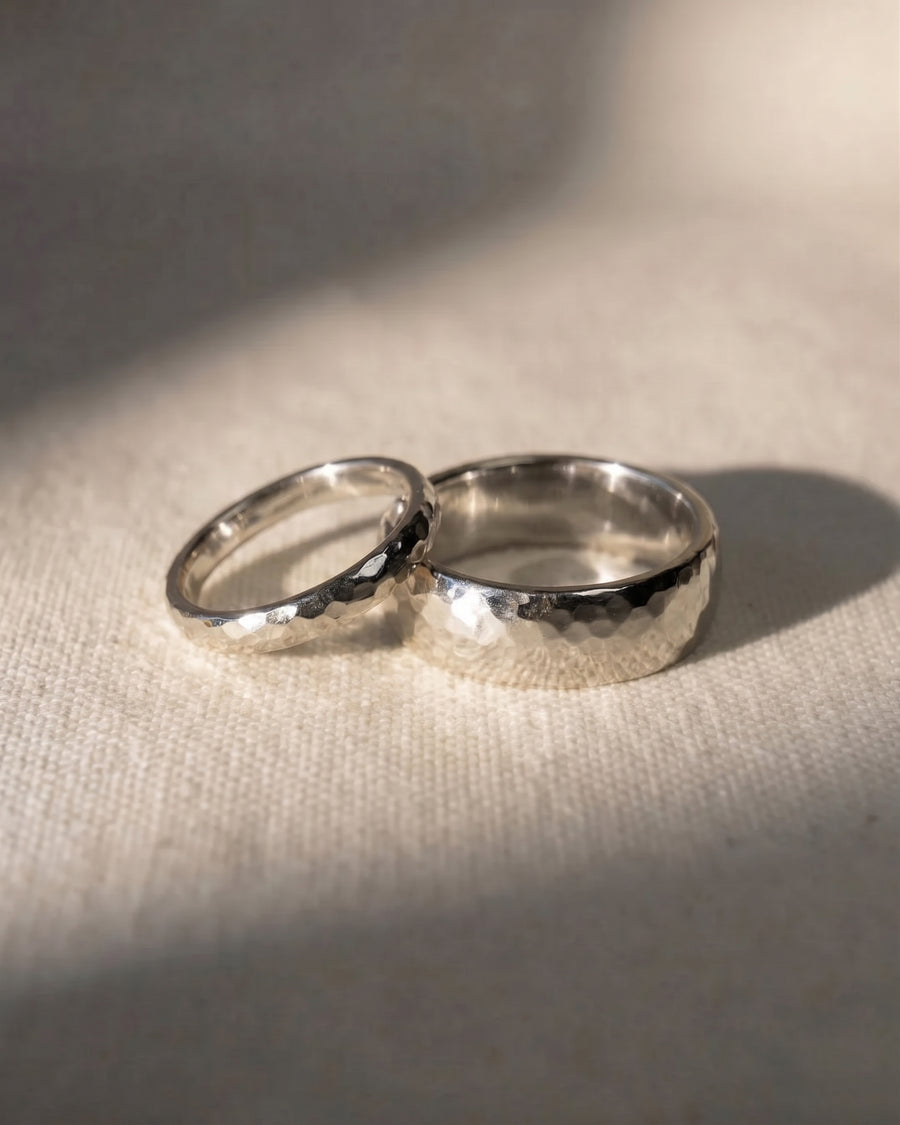 Two platinum hammered court wedding rings resting on a textured fabric surface.