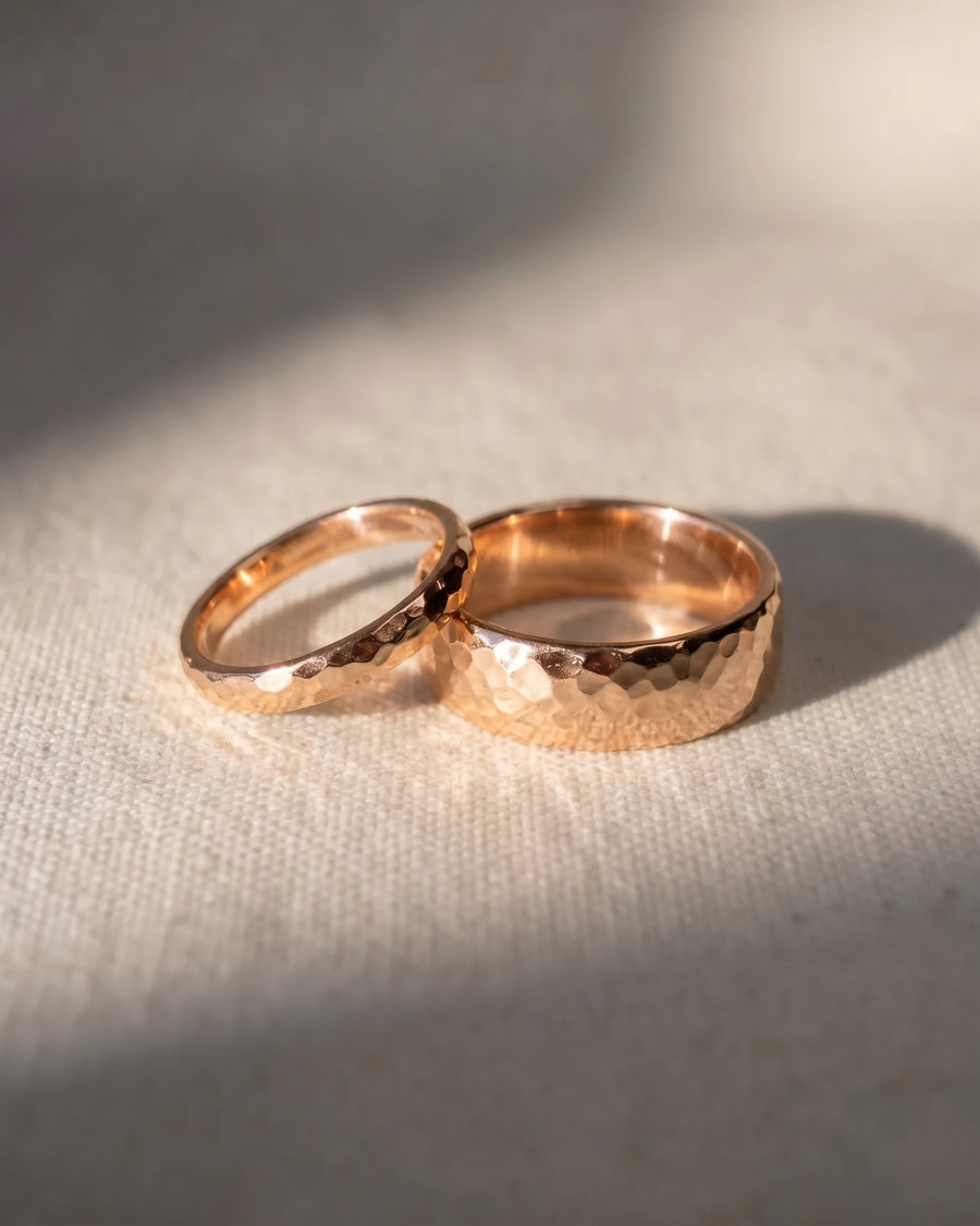 Two rose gold wedding rings with a hammered texture resting on a textured cream surface.