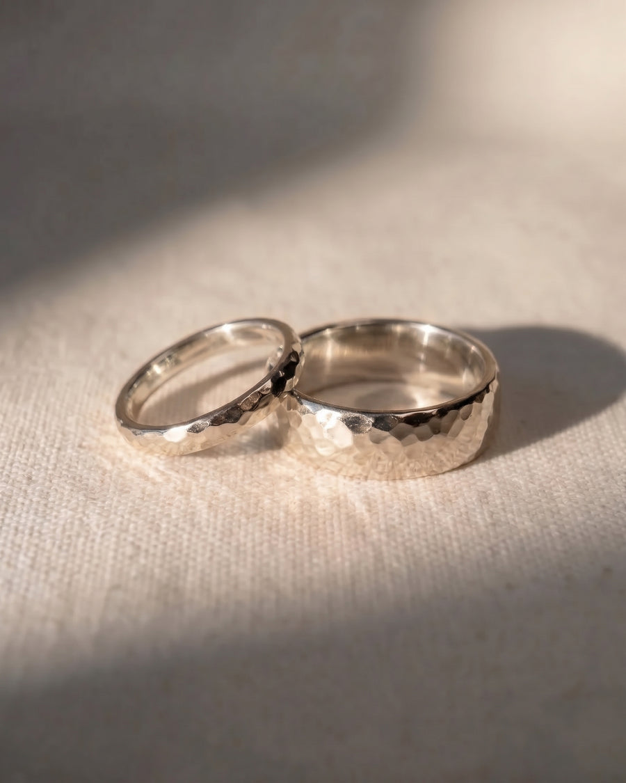 Two 9ct white gold wedding rings with a hammered texture resting on a textured fabric surface.