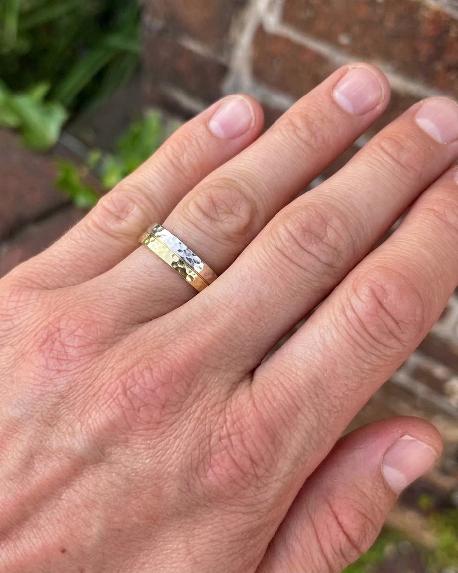 Two-tone gold and silver wedding rings with a hammered texture worn on a finger.